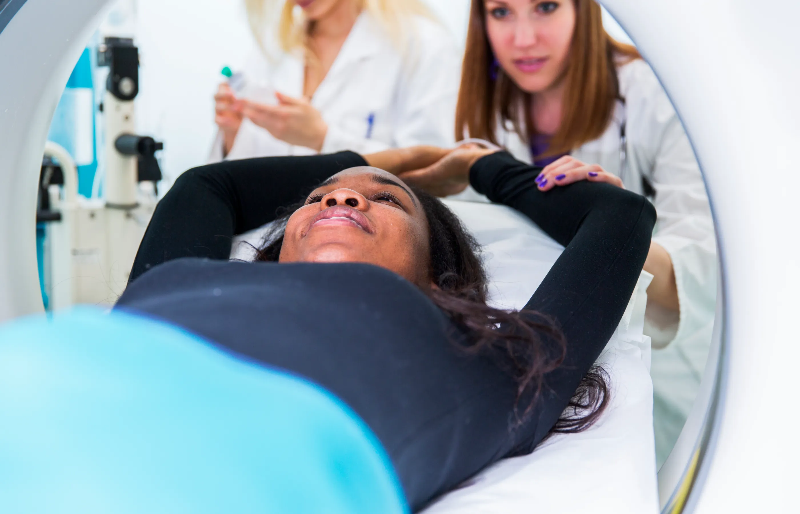 A health care provider is assisting a woman as she is laying down with her arms above her head in an imaging machine. 
