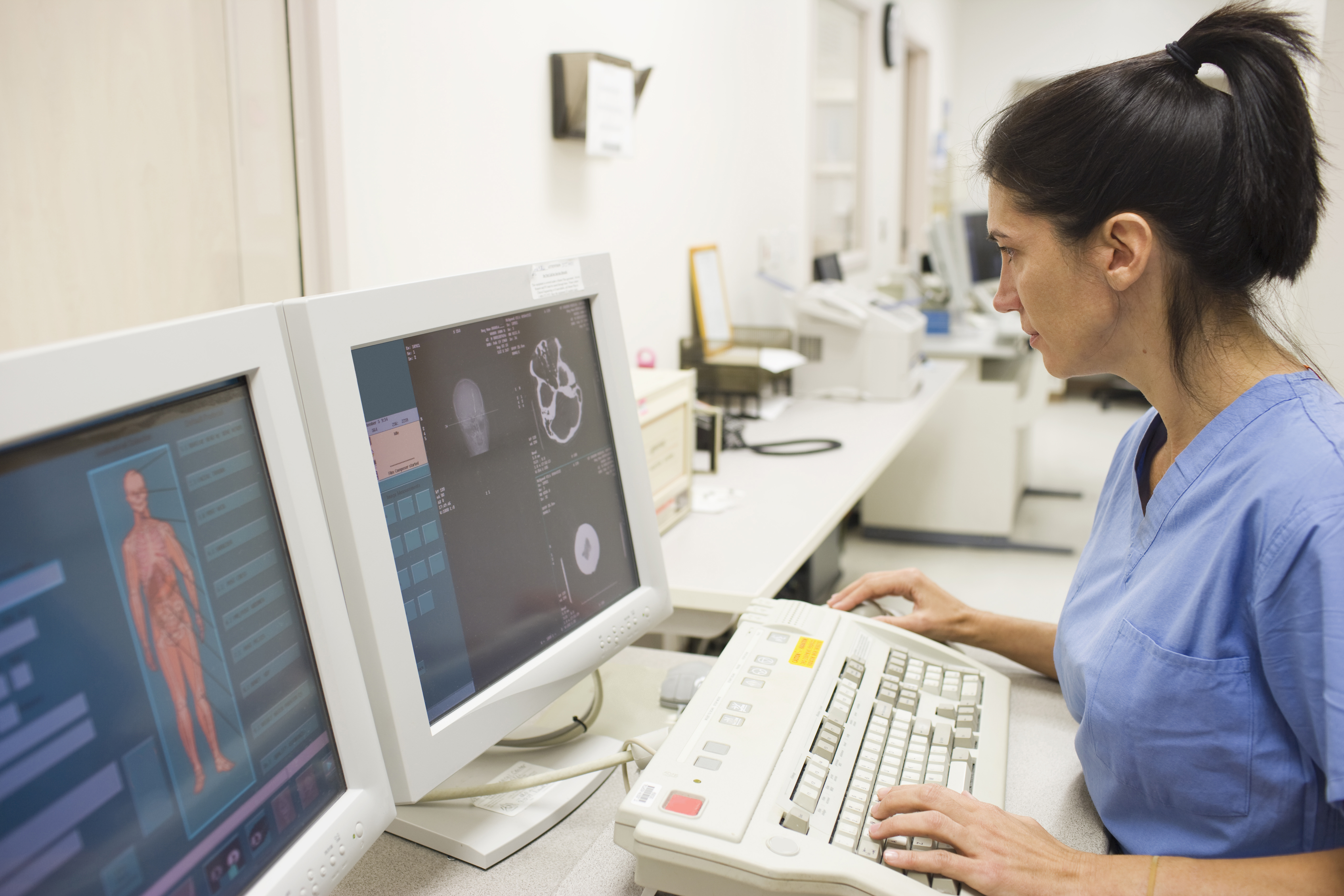 A healthcare provider is reviewing patient imaging scans on two computer monitors. 