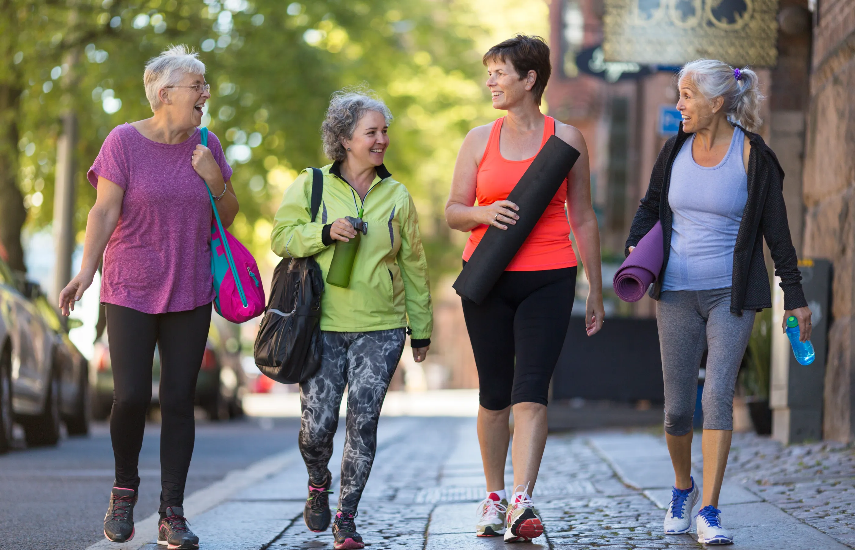 A group of four women are talking and walking together with workout gear in hand. 