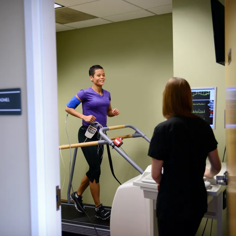 Woman is completing a test on a treadmill as a team member talks to her. 