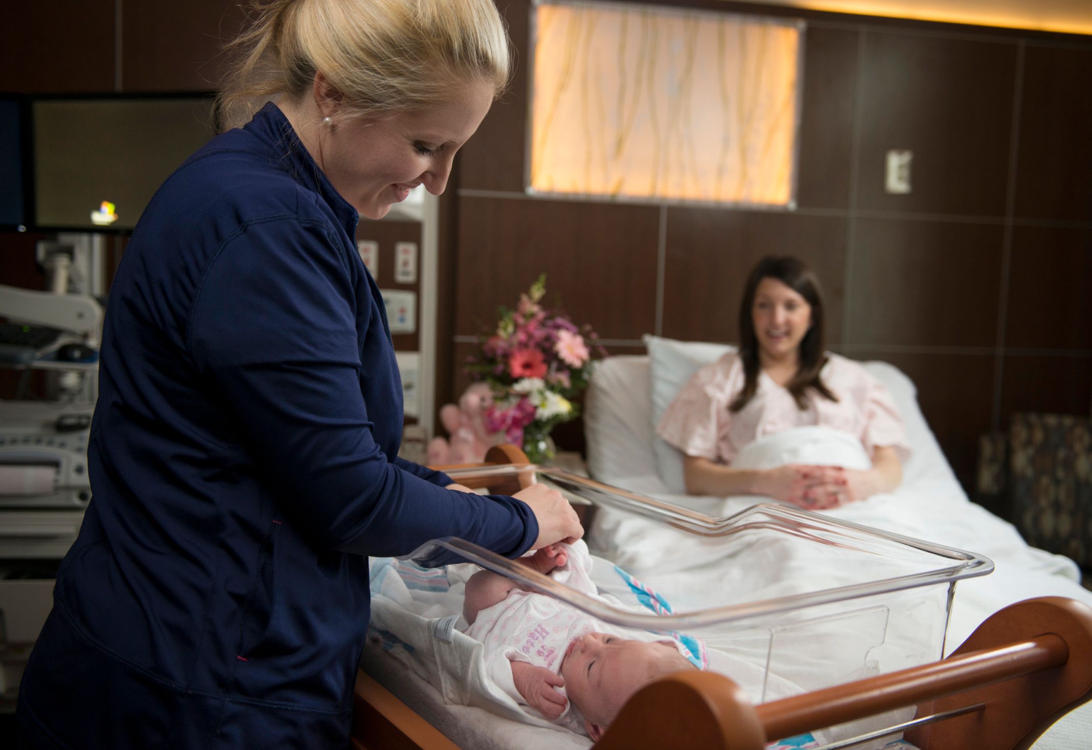 Novant Health nurse tends newborn in bassinet while mom smiles from bed