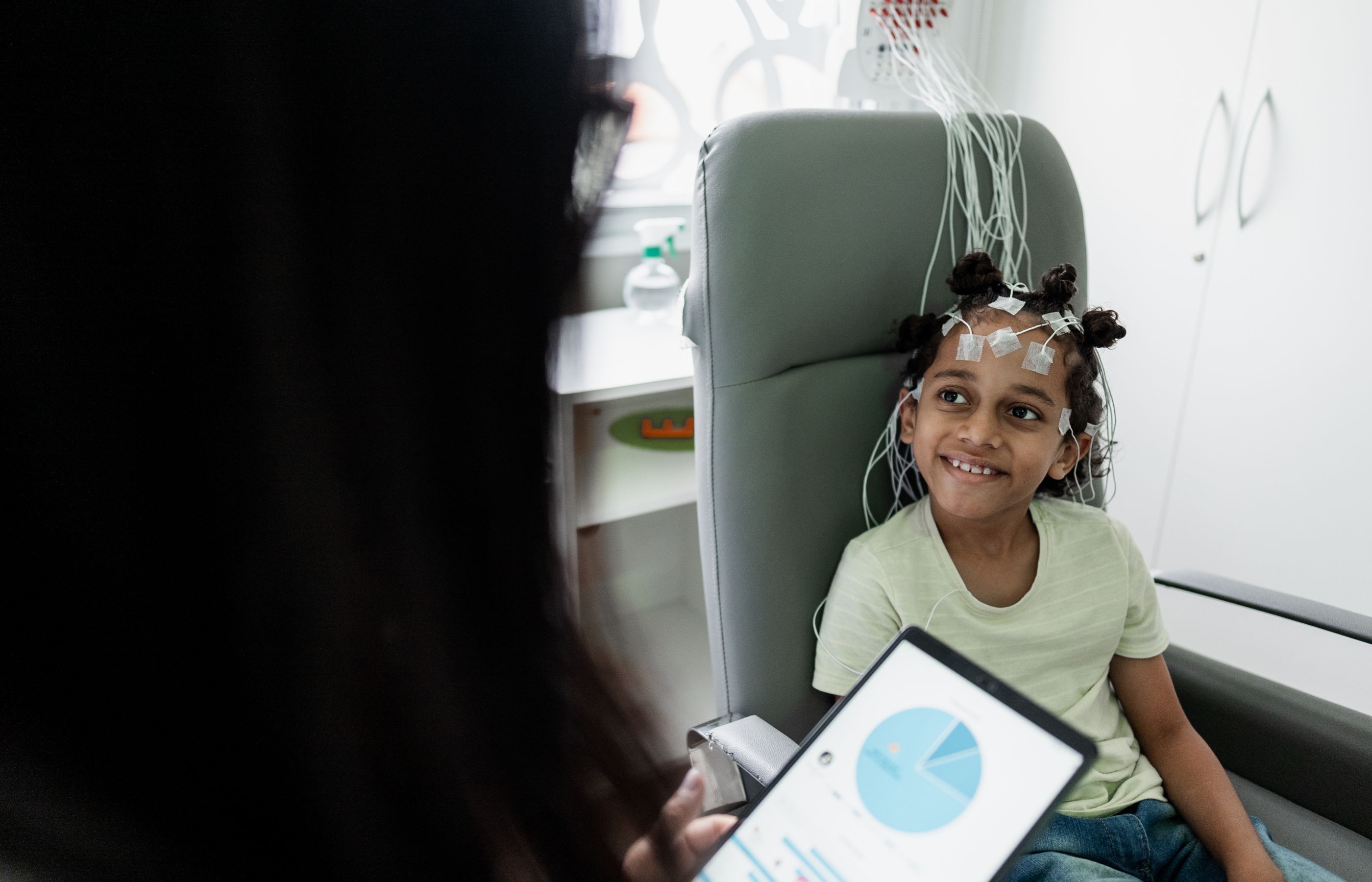 A young girl has sensors on her head as she smiles as her doctor talks with her. 