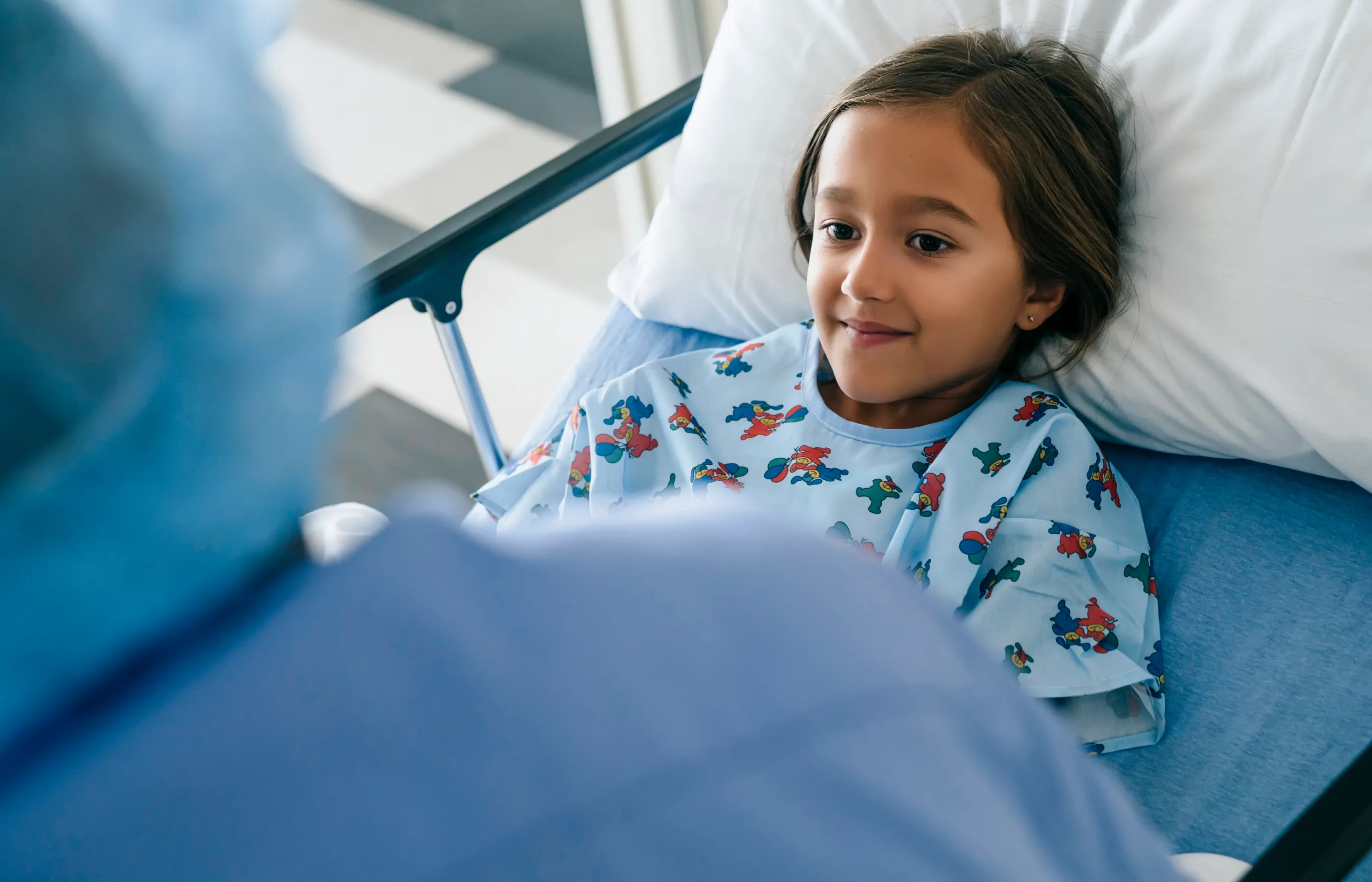 A young child is lying in a hospital bed talking with a health care provider. 