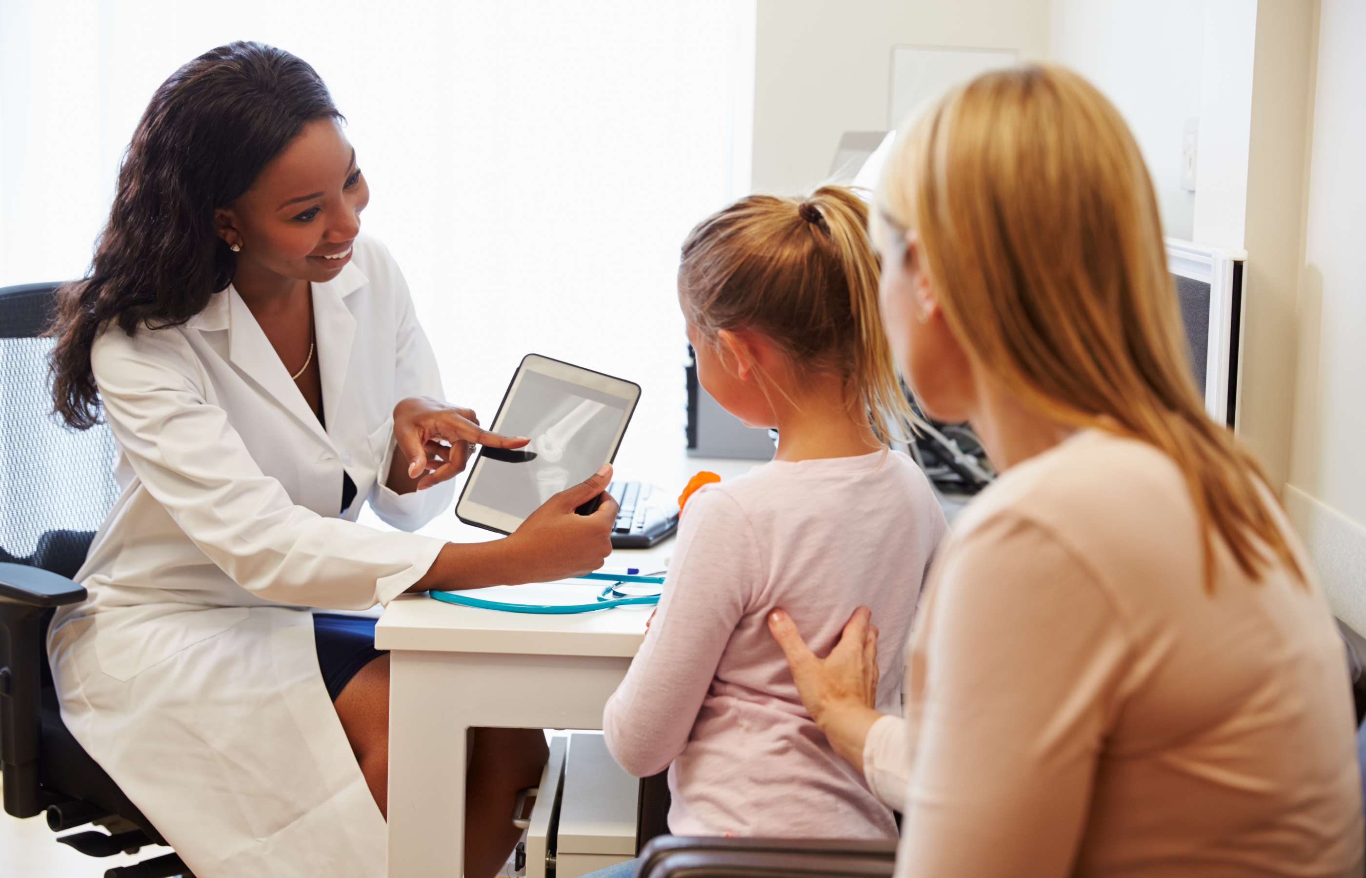 A doctor is reviewing an x-ray scan with a parent and her child. 
