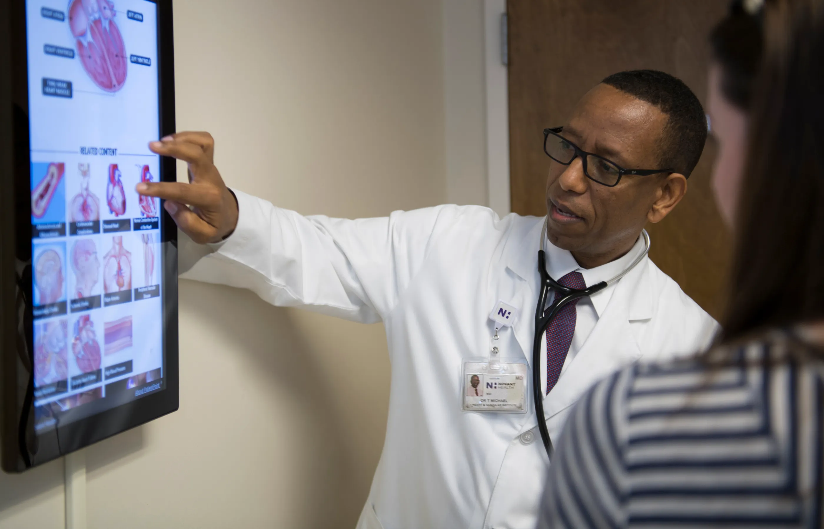 Novant Health's Dr. Michael is using a screen on a wall to display information to a patient. 