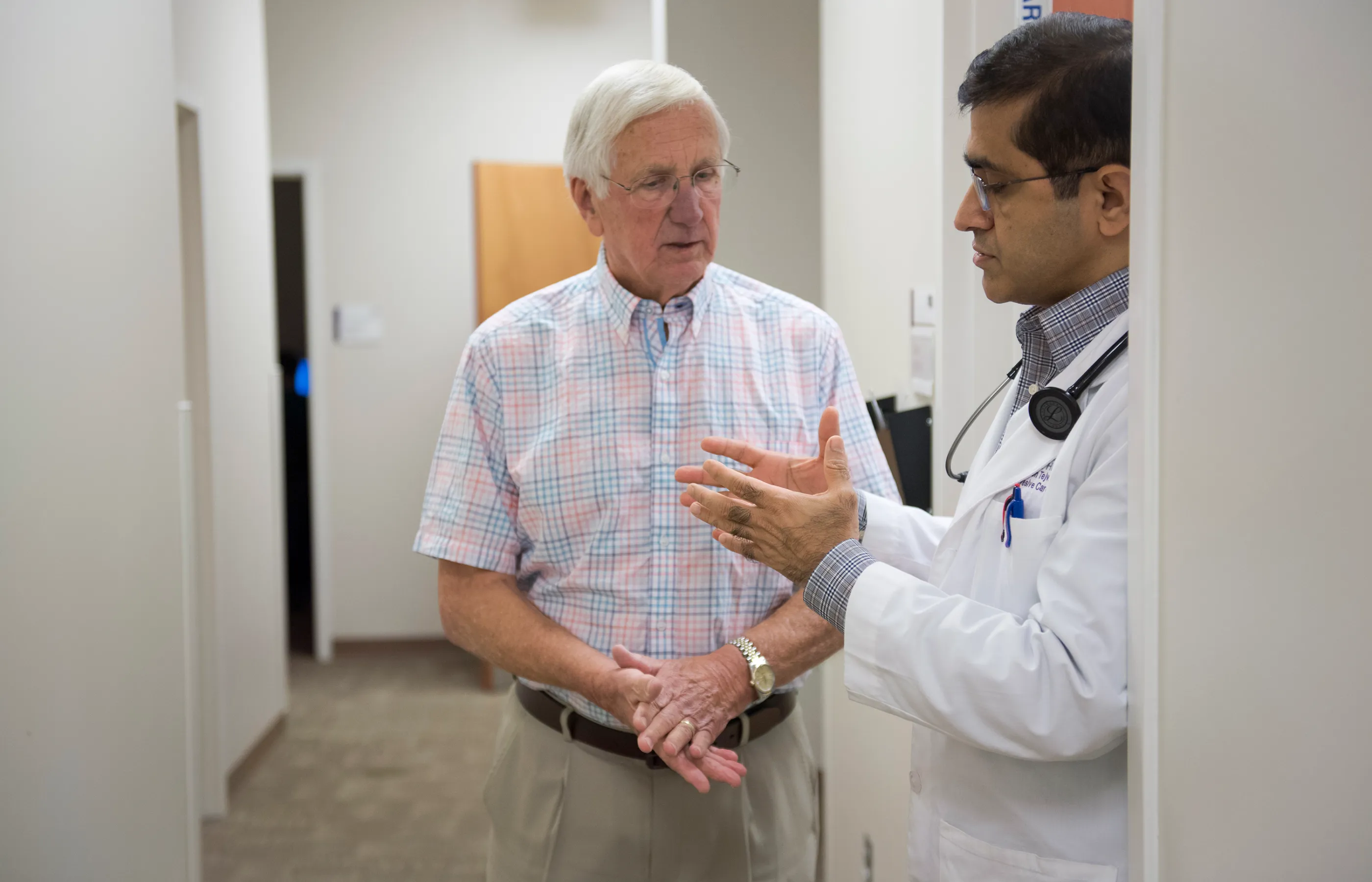 Novant Health's Dr. Tejwani is standing in the hallway of a clinic talking with a patient. 