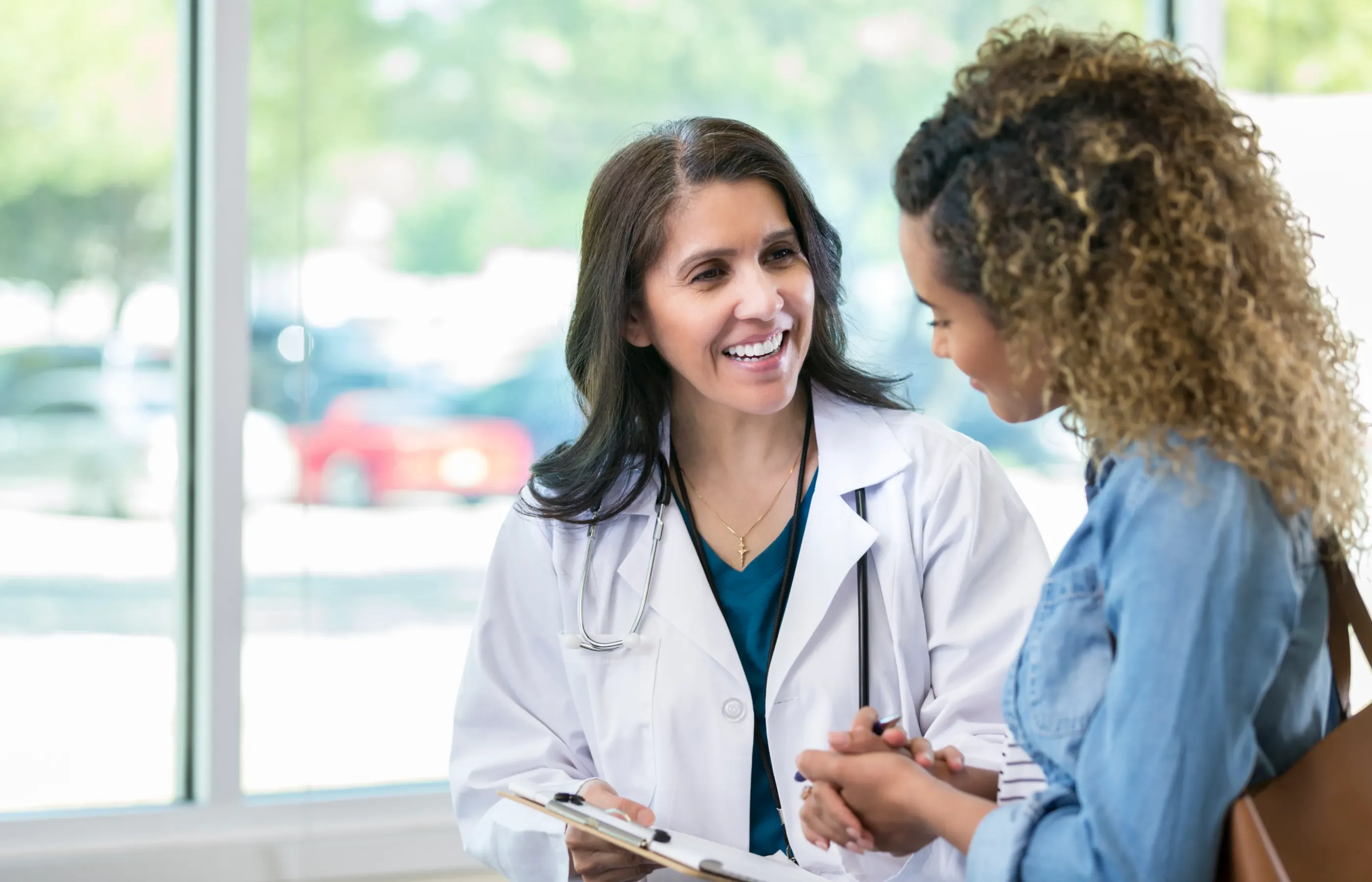 A female provider speaking with a female patient while holding a clipboard.