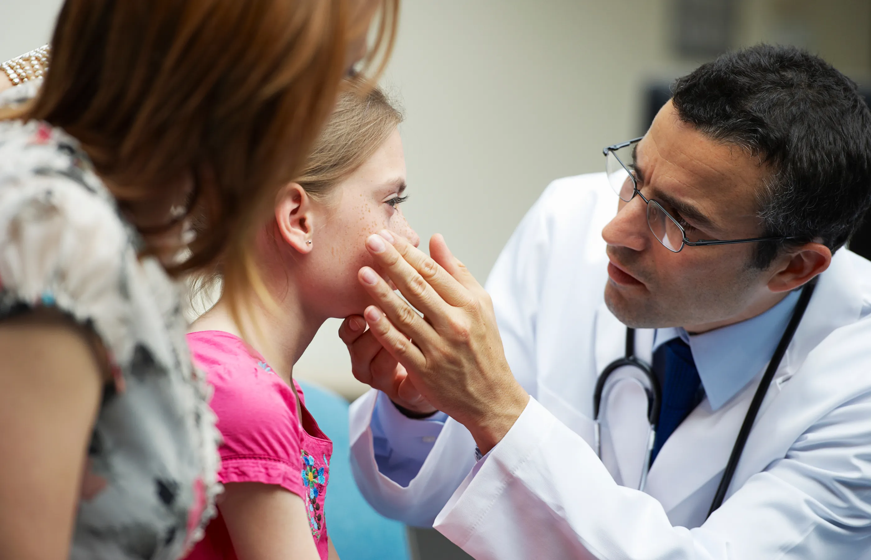 A male doctor exams a little girl's eye while her mother holds her.