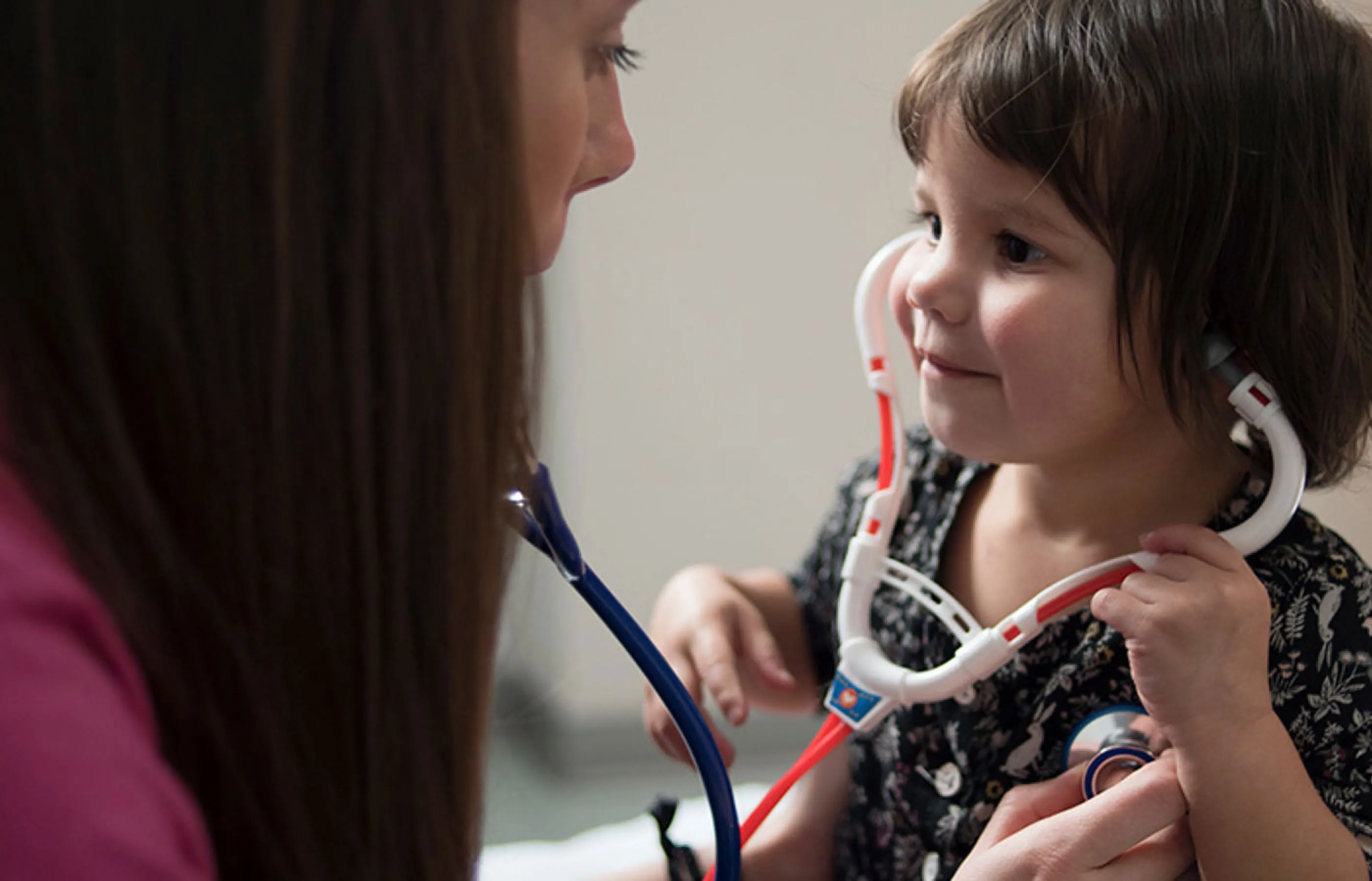A young girl is sitting with a Novant Health nurse as she plays with a toy stethoscope. 