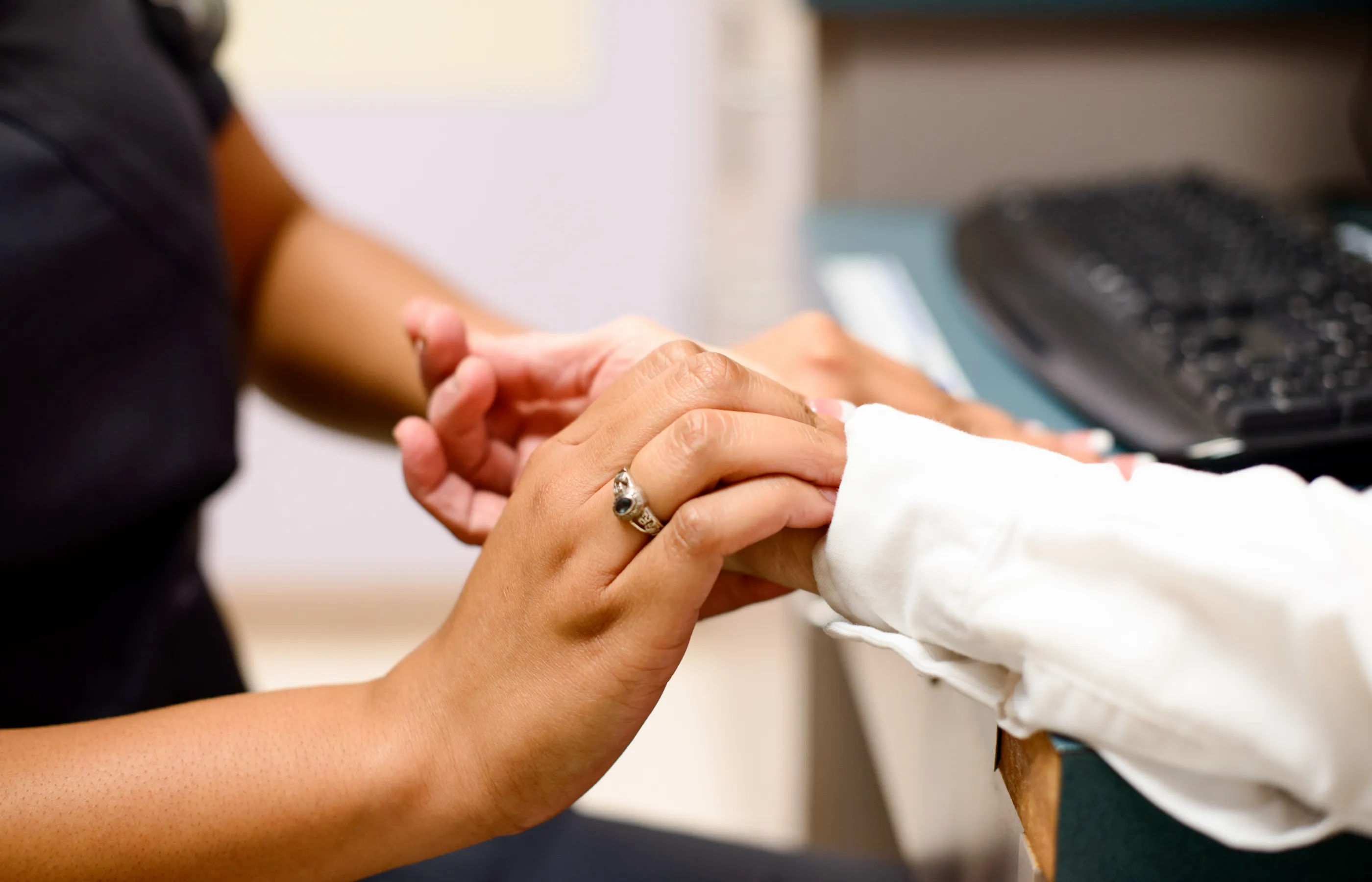 Nurse and patient are sitting across from each other in a clinic exam room. The nurse holds and positions the patients hands to check for their pulse. 