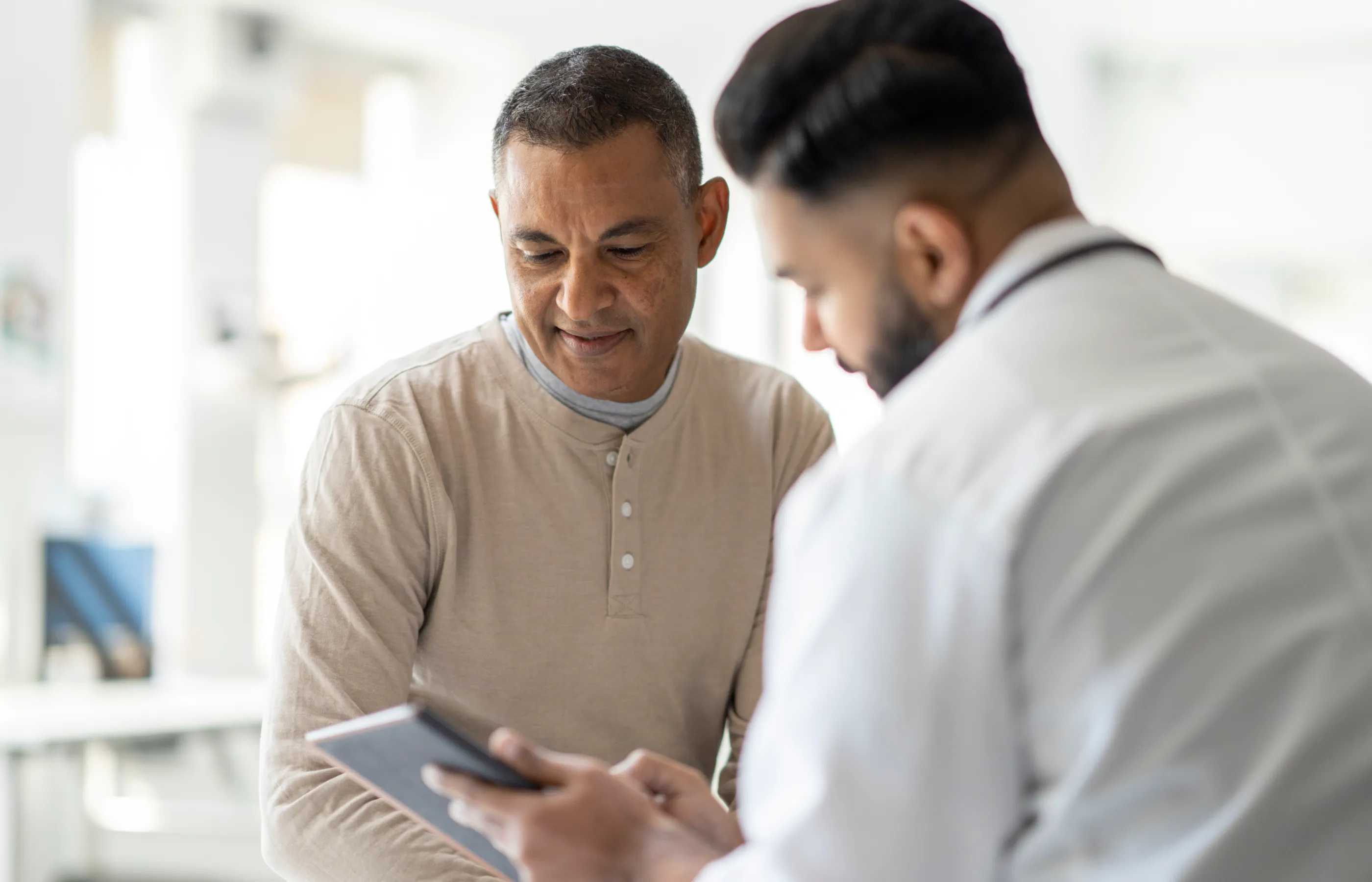 A male doctor reviews a list with a male patient in an exam room.