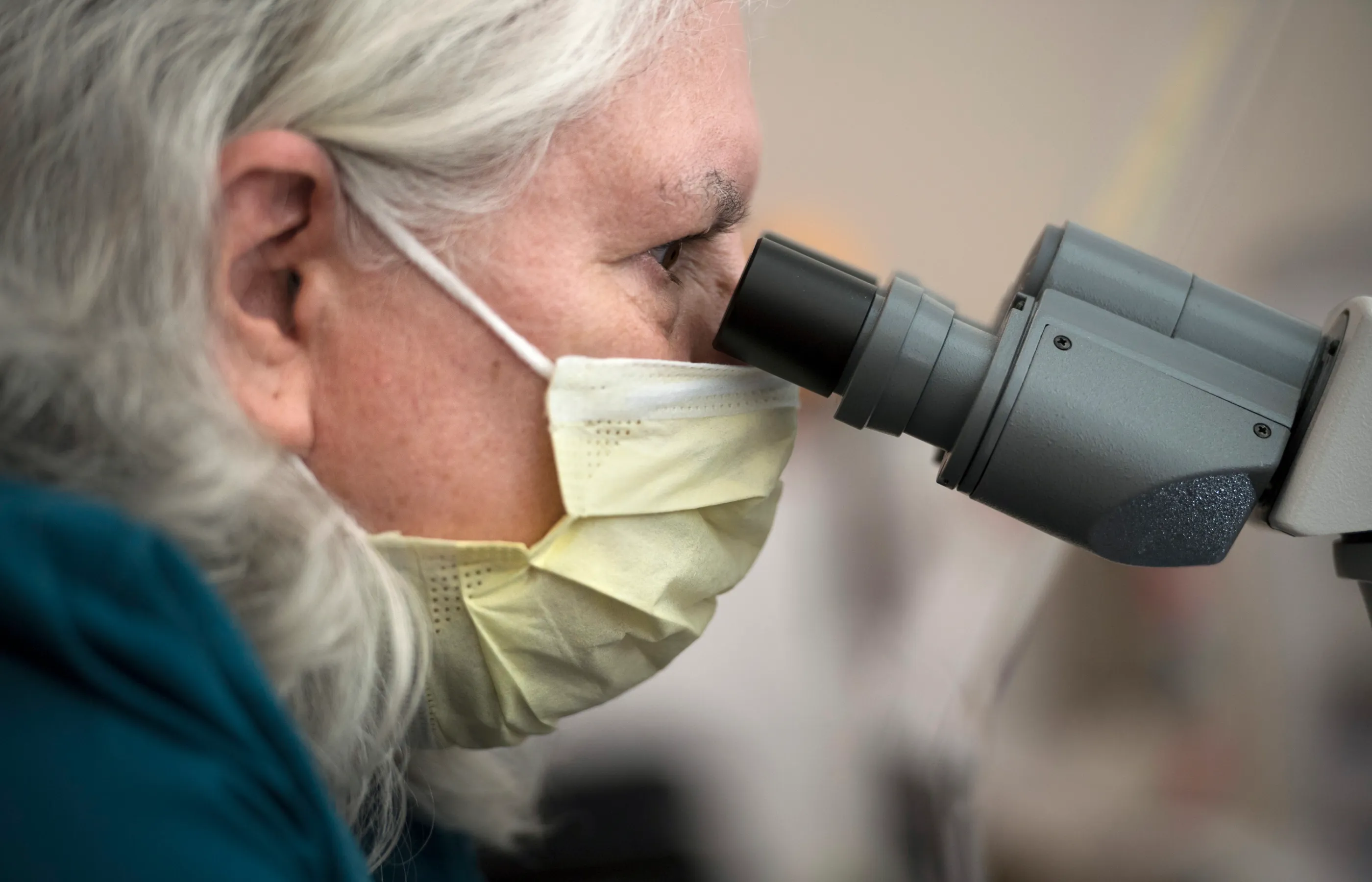A Novant Health team member is in a lab looking through a microscope. 