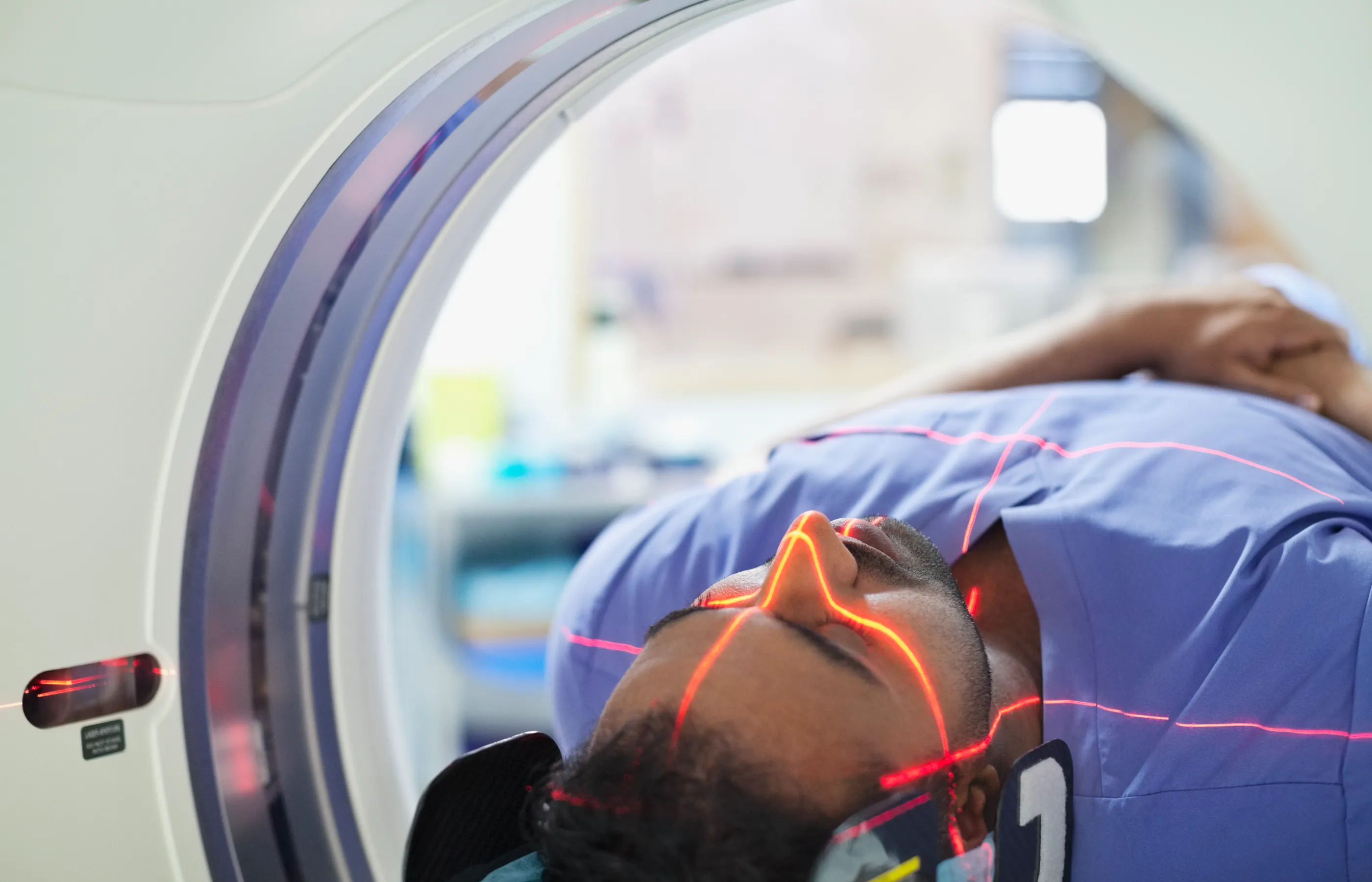 A patient having an MRI scan completed. They are lying down in the machine with their eyes closed as the machine beams light along their face and body. 