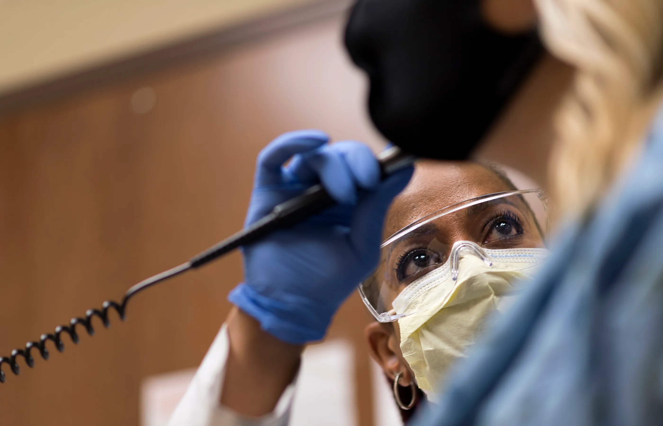 A masked Novant Health doctor is evaluating a patient's ear with a scope and light.
