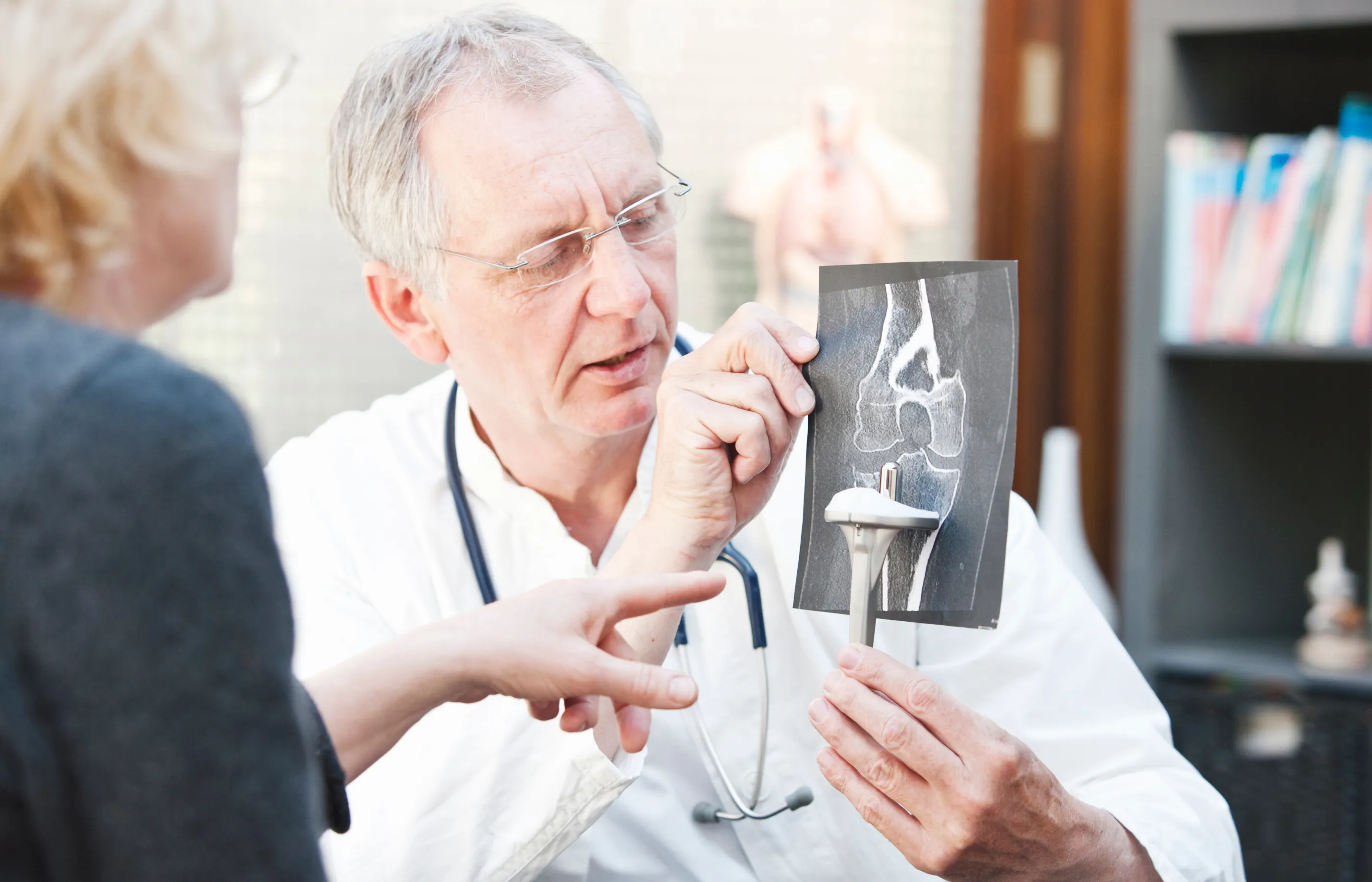 A doctor explains an X-ray to a patient using a model bone