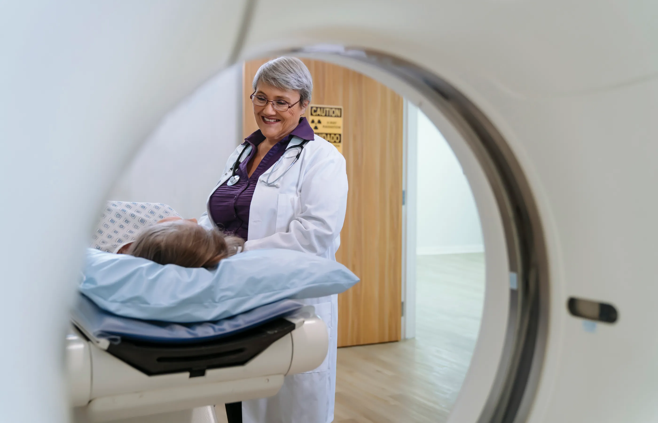 A doctor is talking with a patient as they lie down preparing for an imaging scan. 