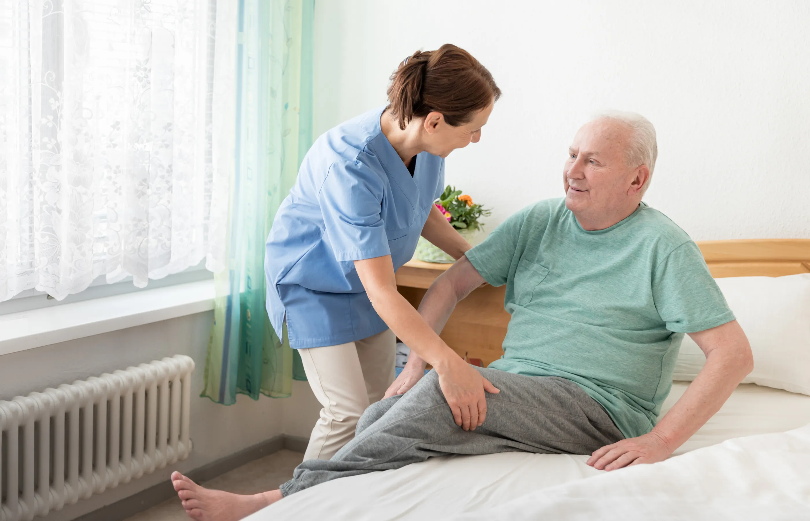 A nurse is assisting a senior man as he sits up in bed. 