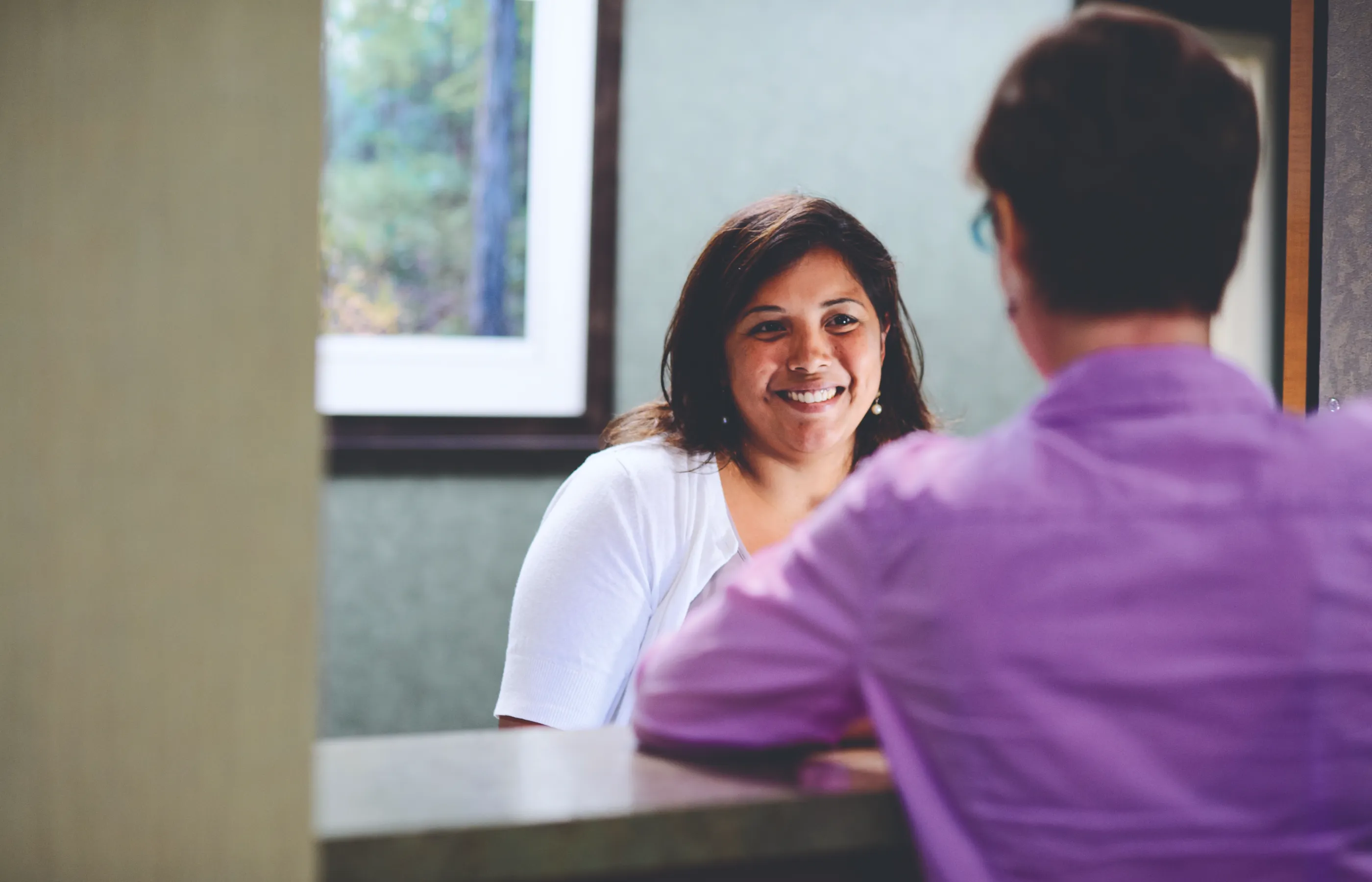 A Novant Health team member is smiling at a patient at the front desk of a clinic. 