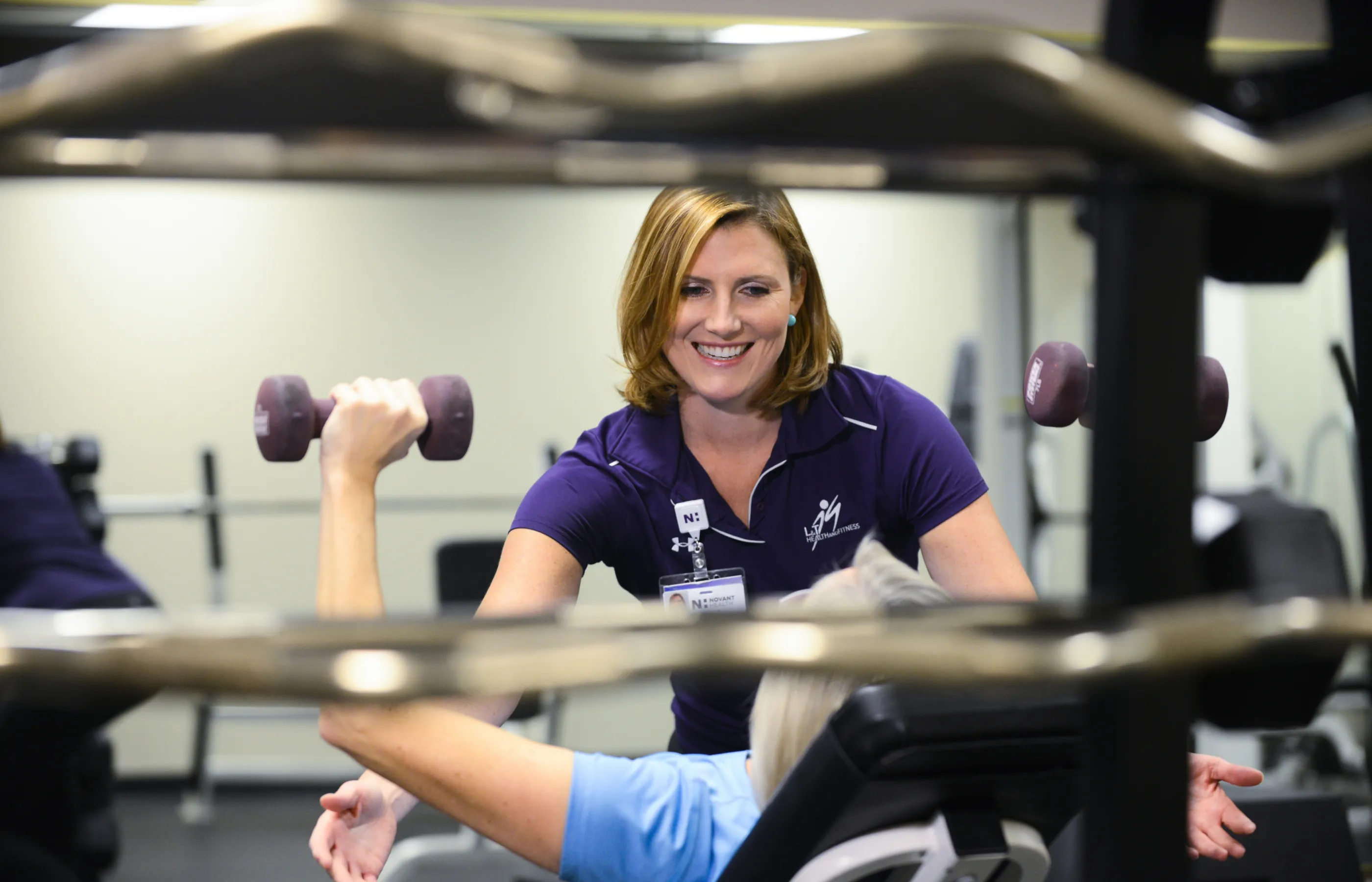 A Novant Health physical therapist is spotting a patient as they lift weights. 