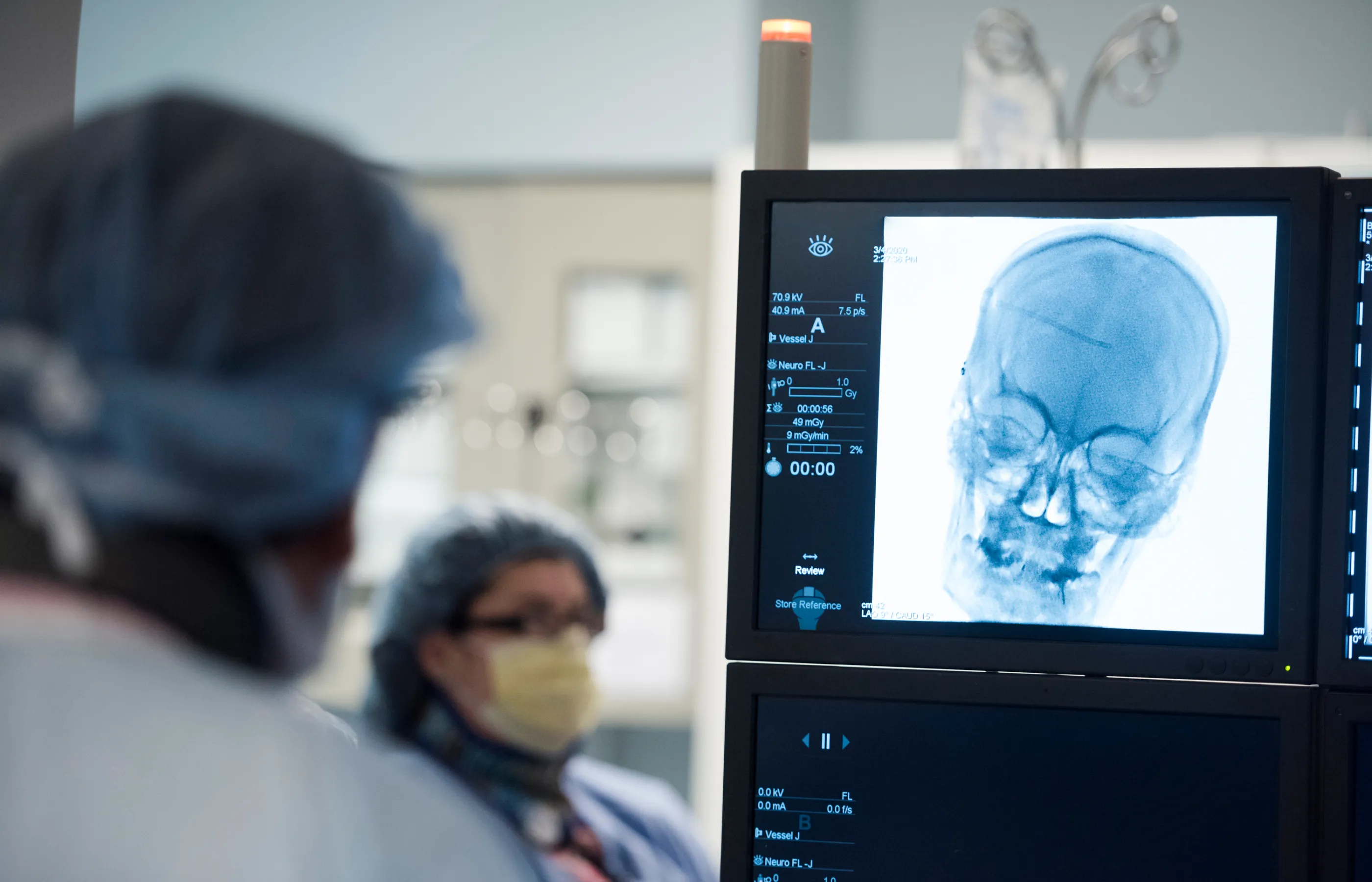 Two Novant Health team members are in surgery. One is looking at a computer monitor, that has an image of the patients skull on it. 