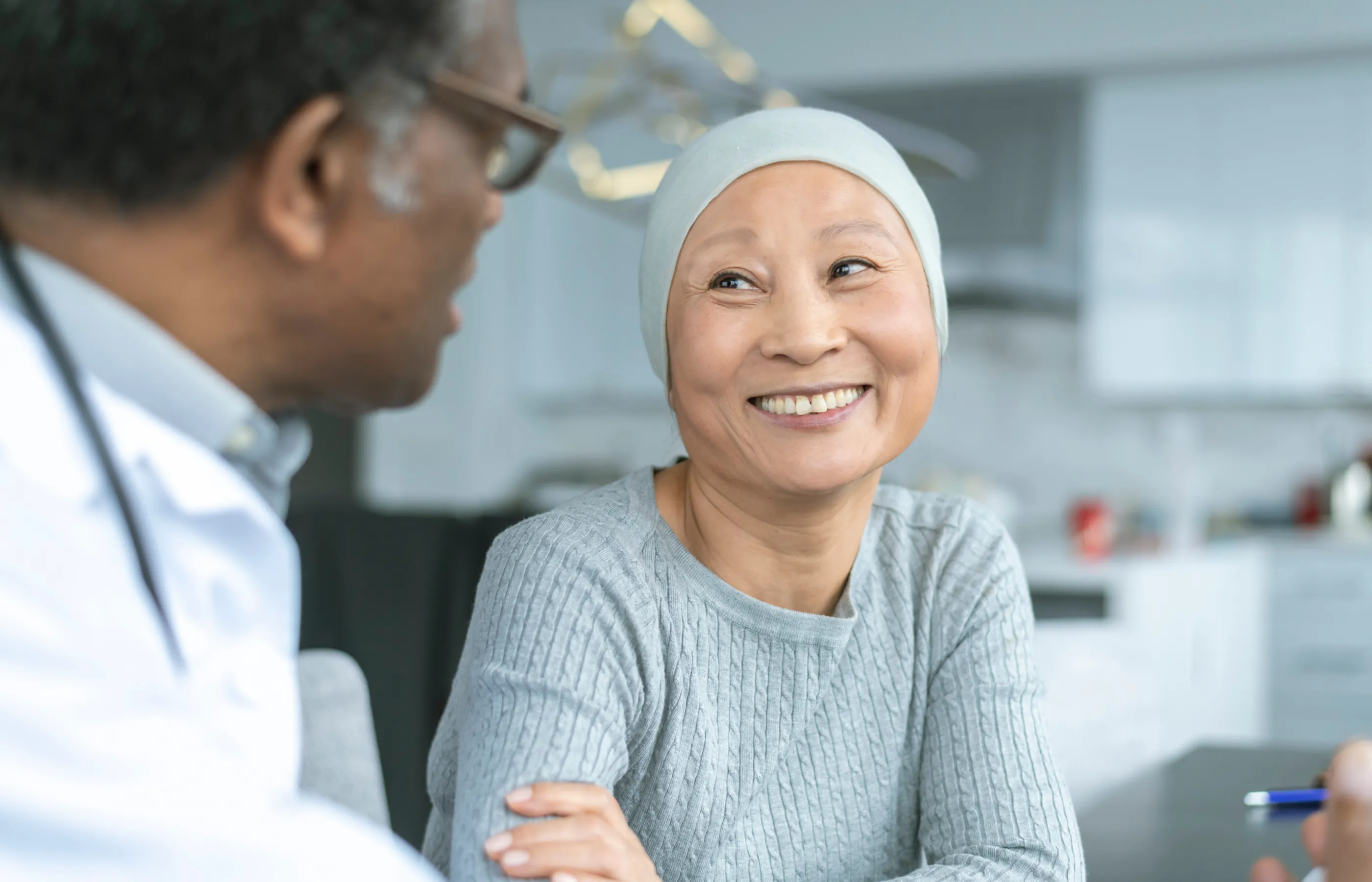 A cancer patient is sitting, smiling, and talking with her healthcare provider. 