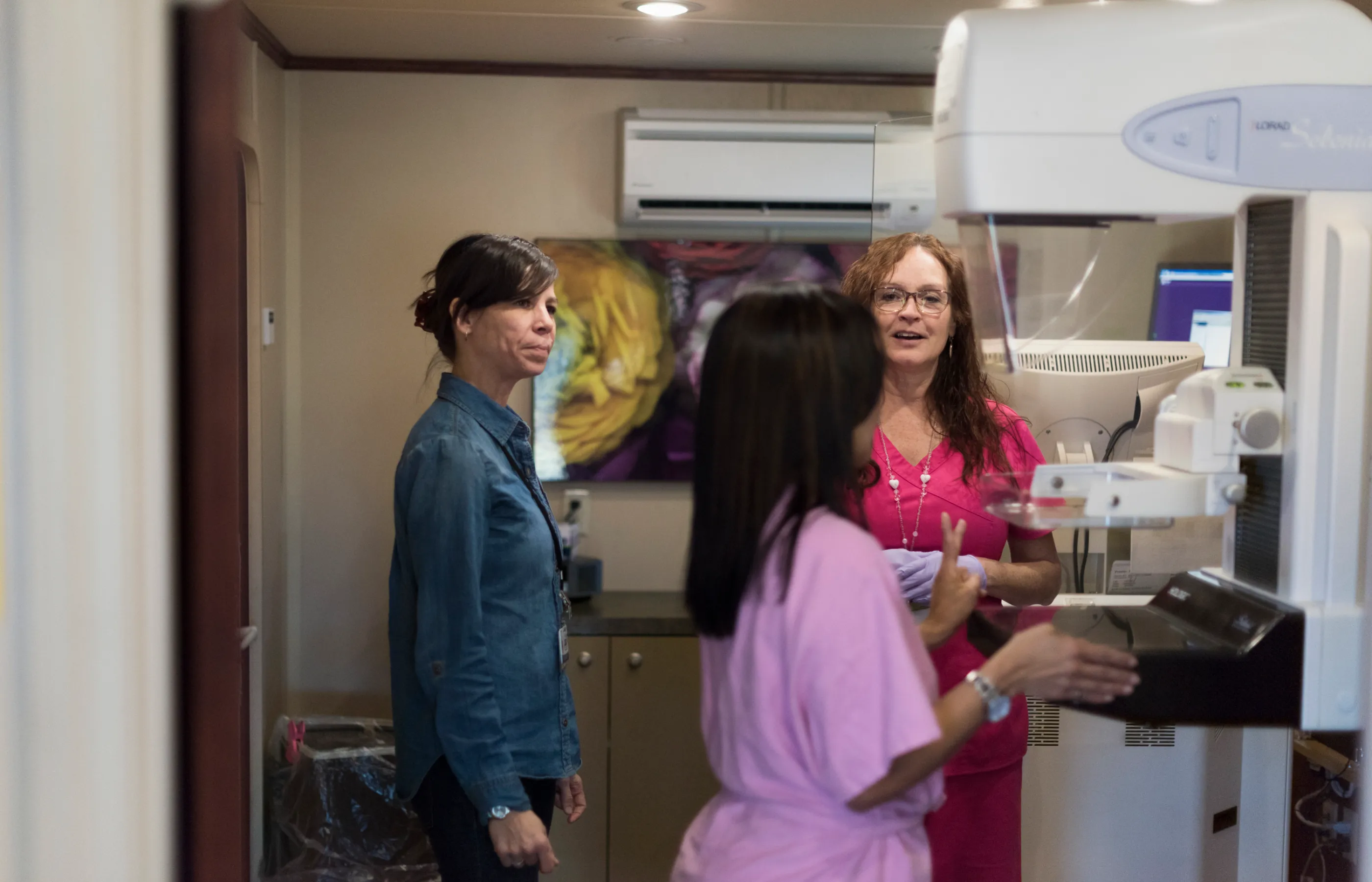 Two team members and a woman are preparing for a mammography scan. 