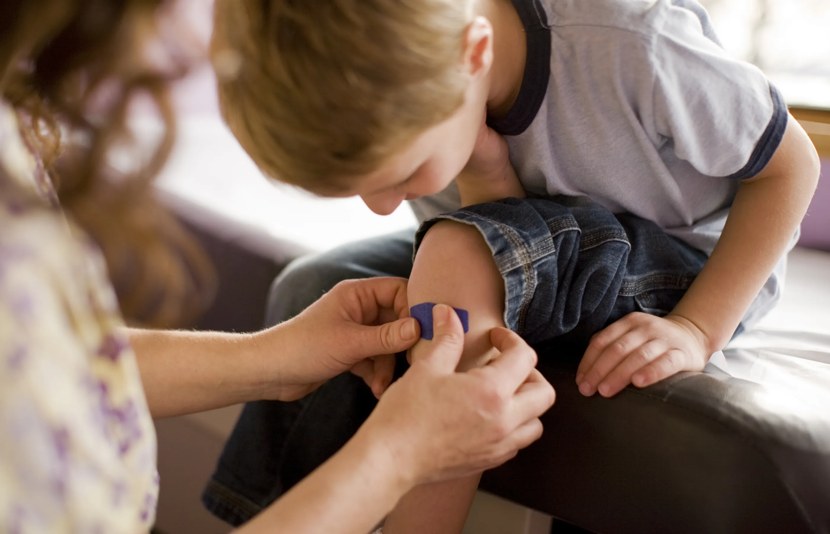 A mom is putting a band-aid on her young sons knee. 