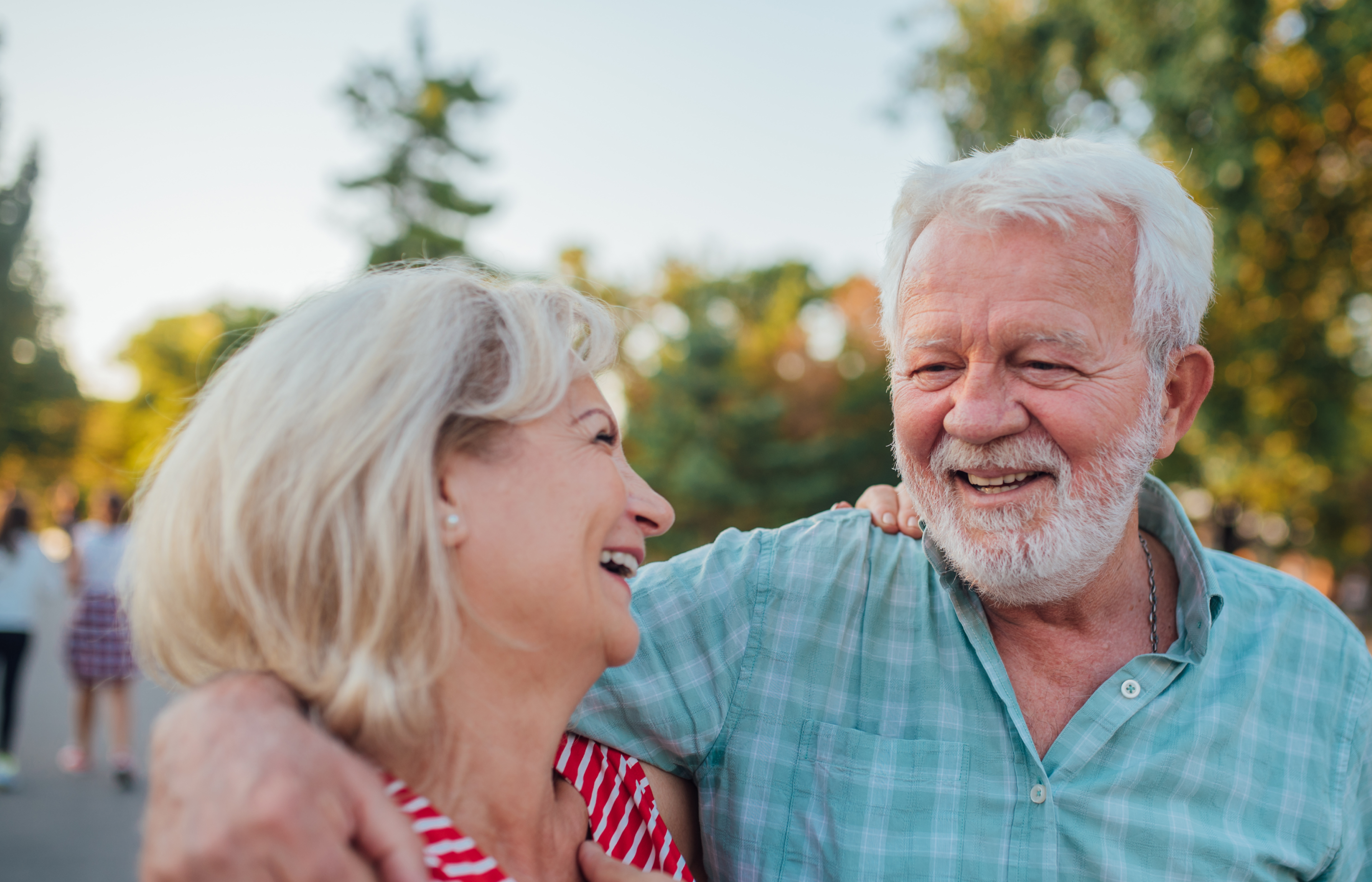 An older couple smiling and laughing together in a park, enjoying a sunny day.