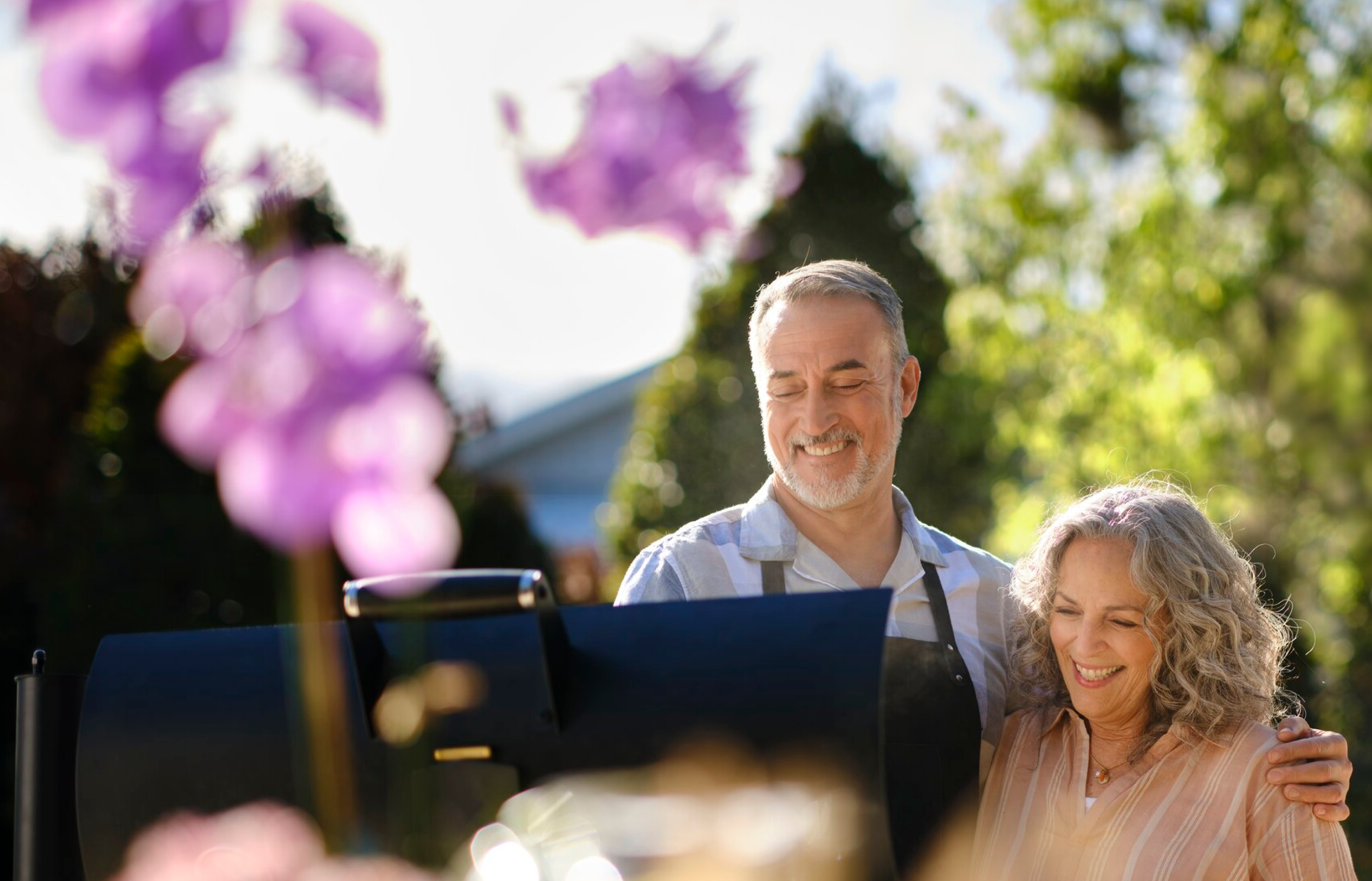 A couple stands outdoors behind a grill.