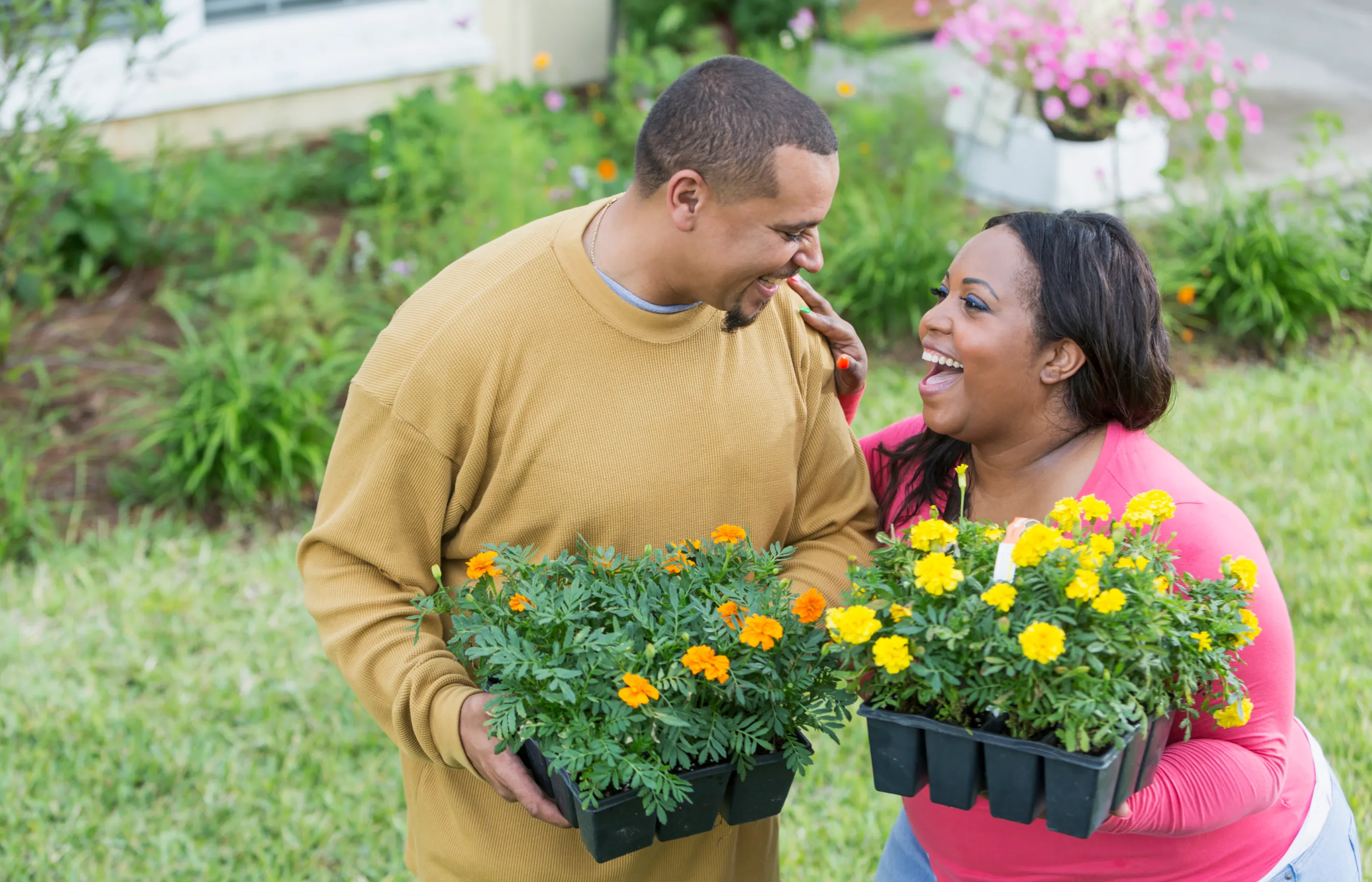 A couple is standing in their yard, preparing to plant flowers and laughing. 