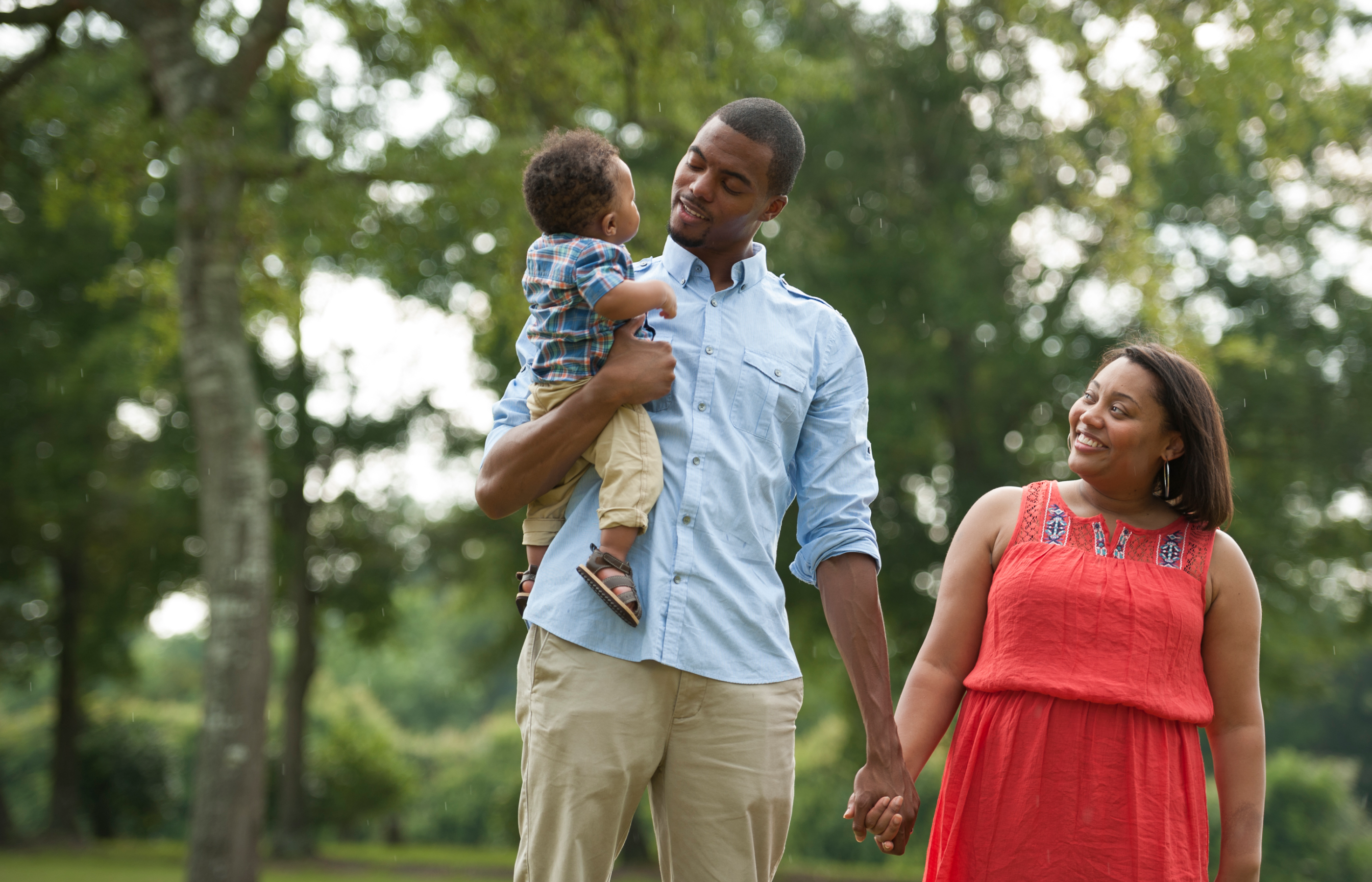 A couple smiling while walking outside with their baby.