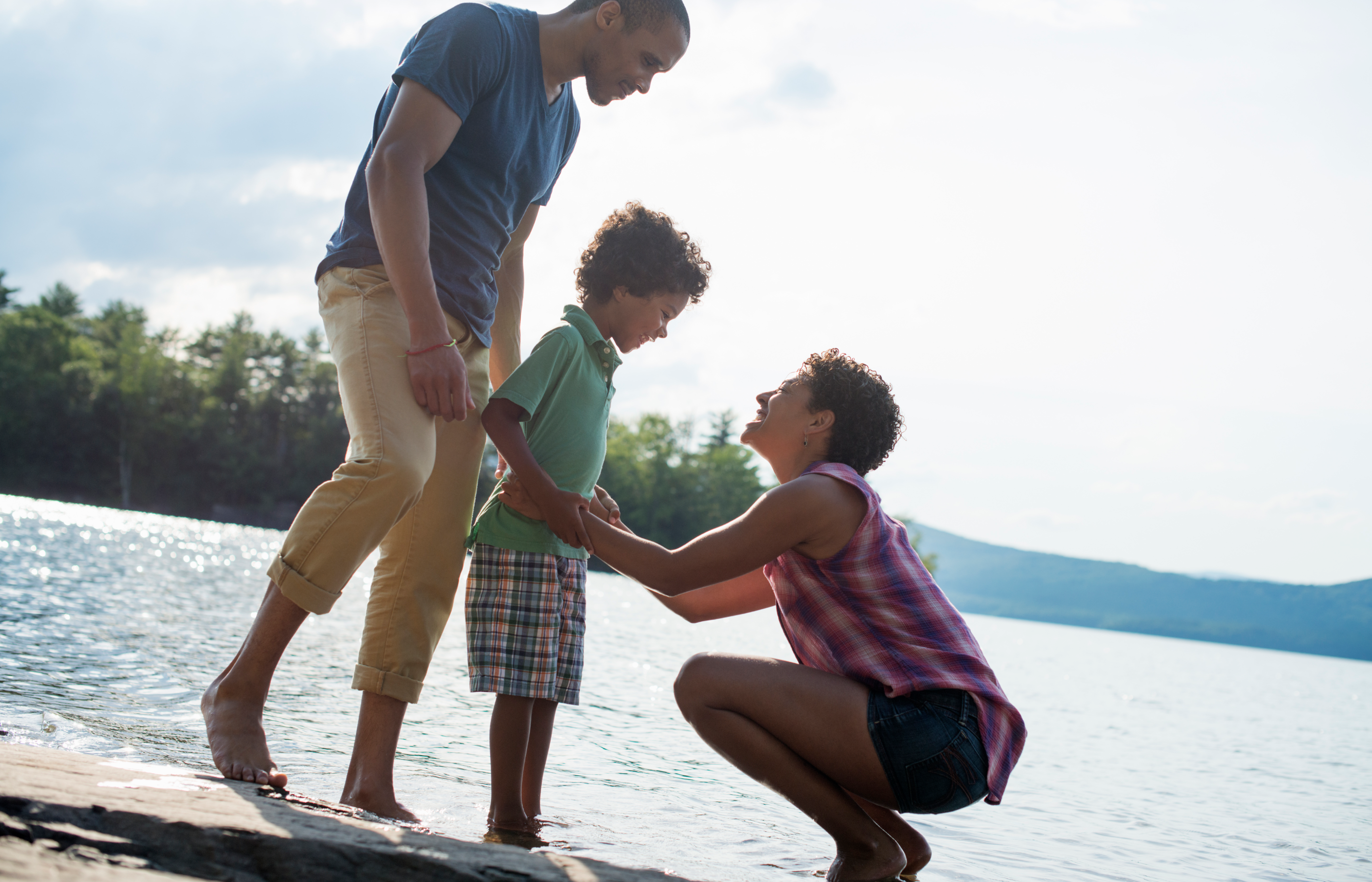 A family at the beach standing in the sand next to the water on a sunny day.