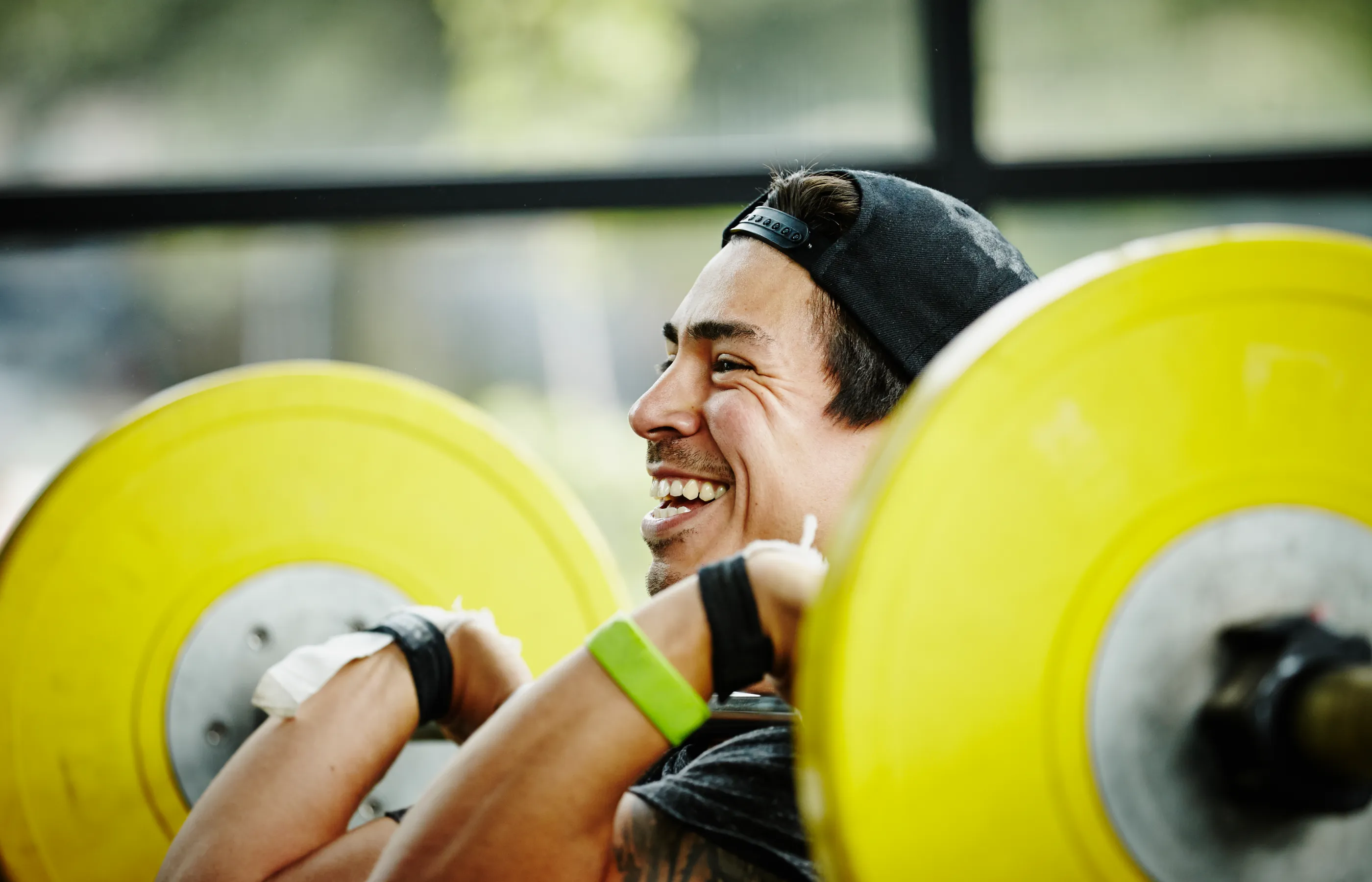 A man is smiling as he lifts heavy weights on a bar bell. 