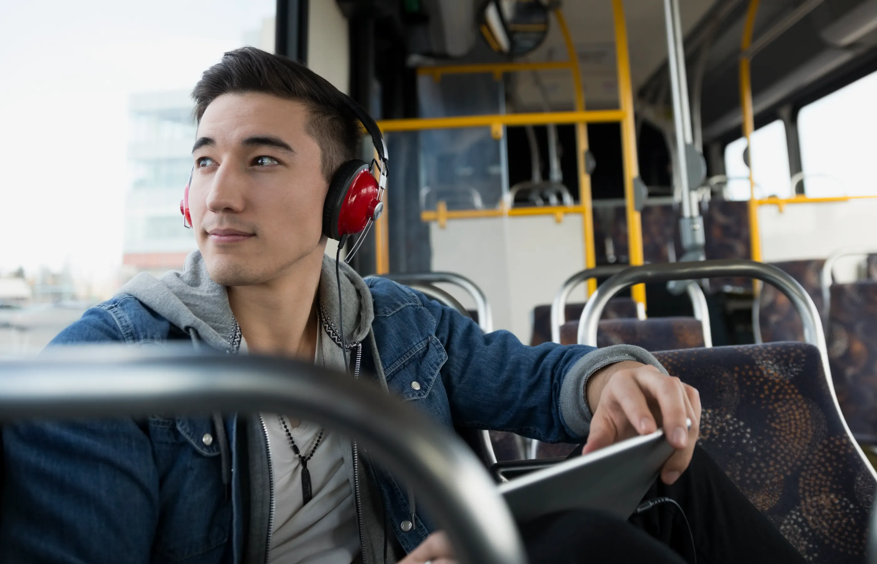 Young man sitting on a public bus with headphones on a tablet in hand. 
