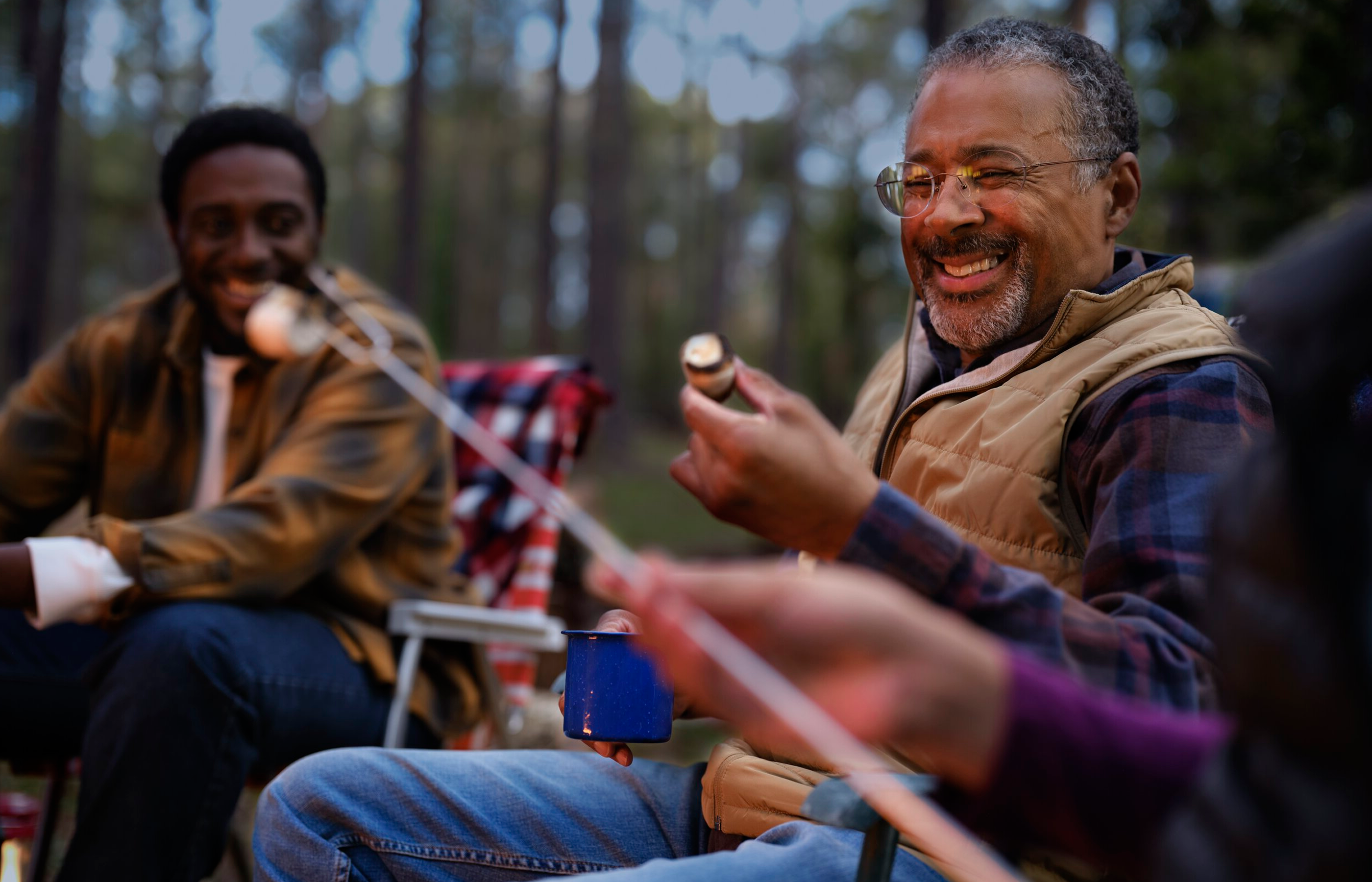 A group of men outdoors by a campfire making smores.
