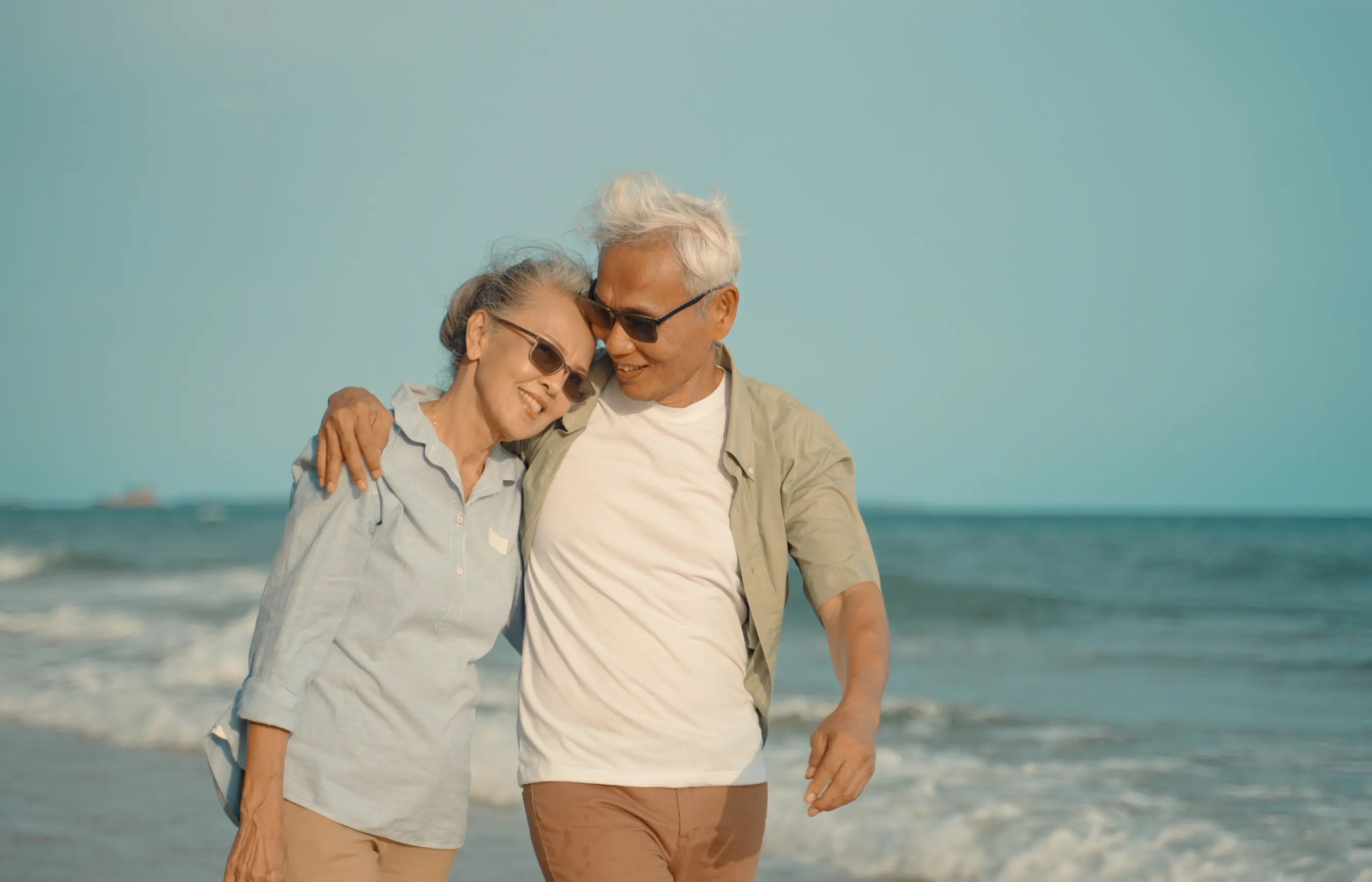 A senior couple are embracing each other as they walk along the beach. 