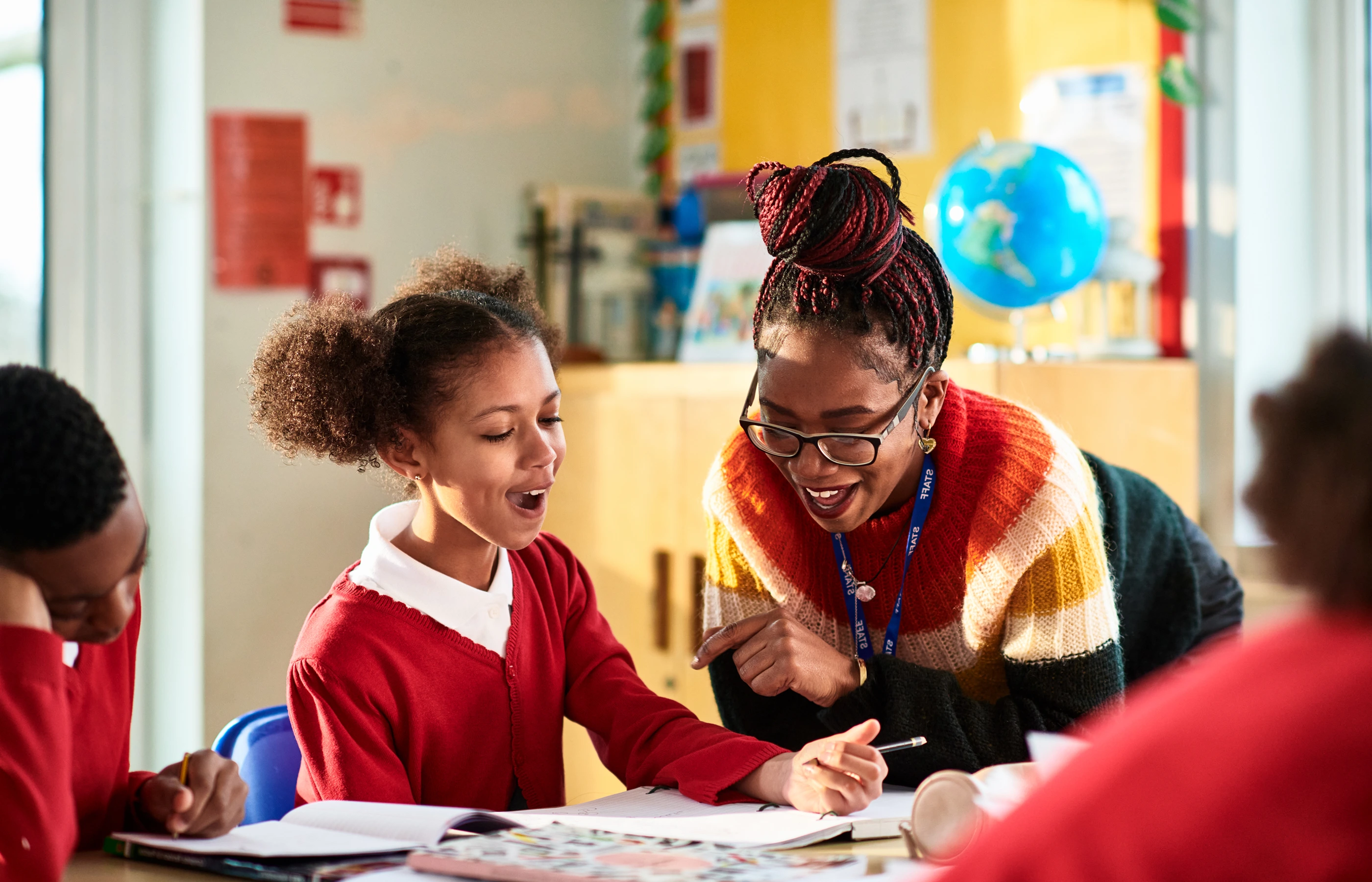 K-12 teacher smiling as she helps an excited student in her classroom