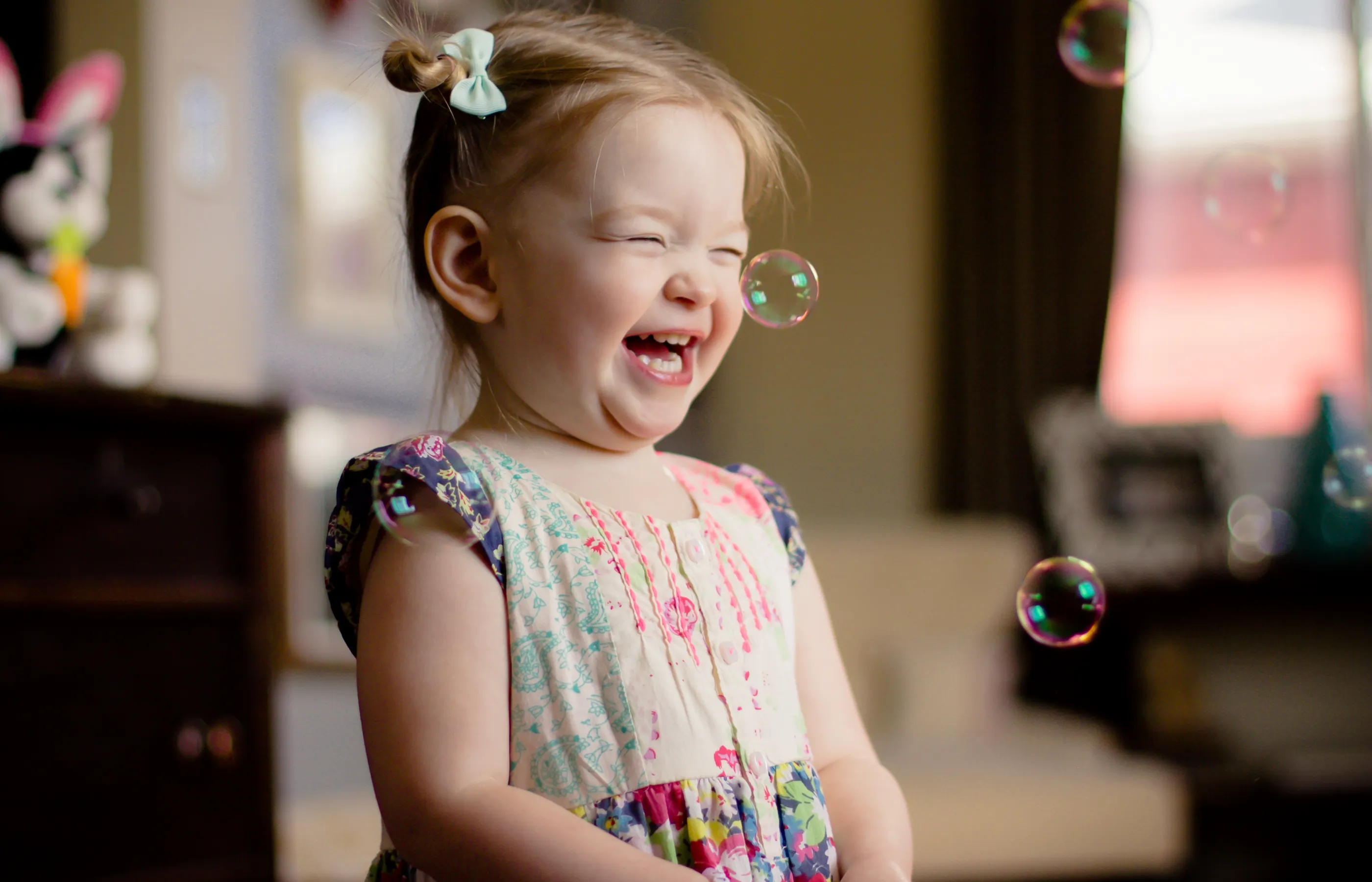 A young toddler girl is laughing as she plays with bubbles. 