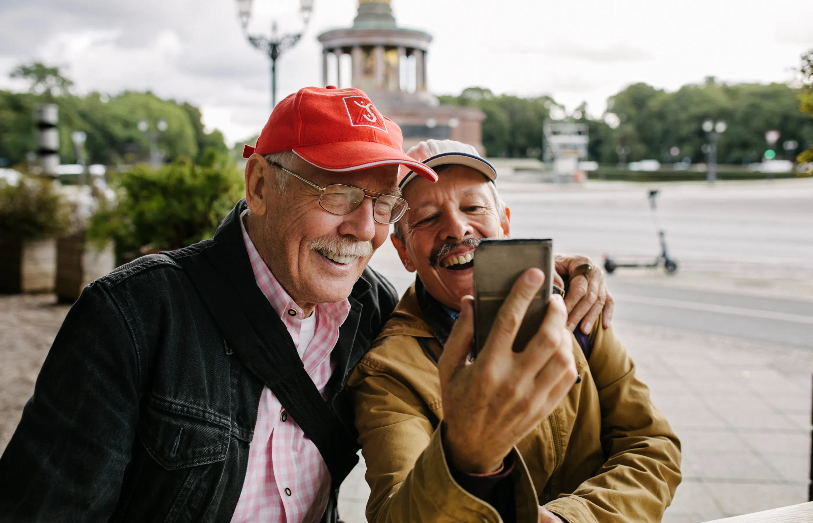 Two senior men are taking a selfie in front of a landmark.