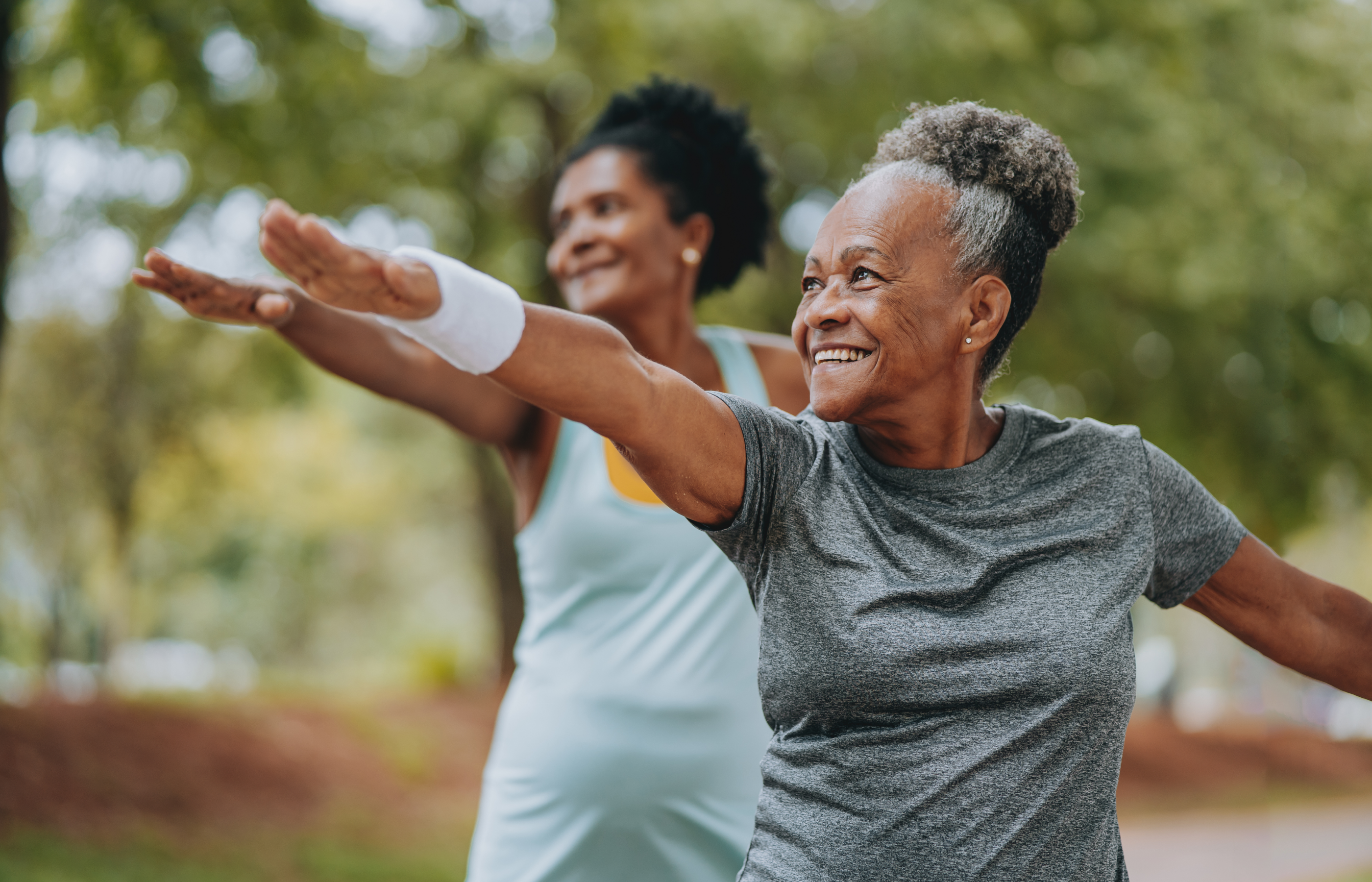 Two women are outdoors stretching and practicing yoga. 