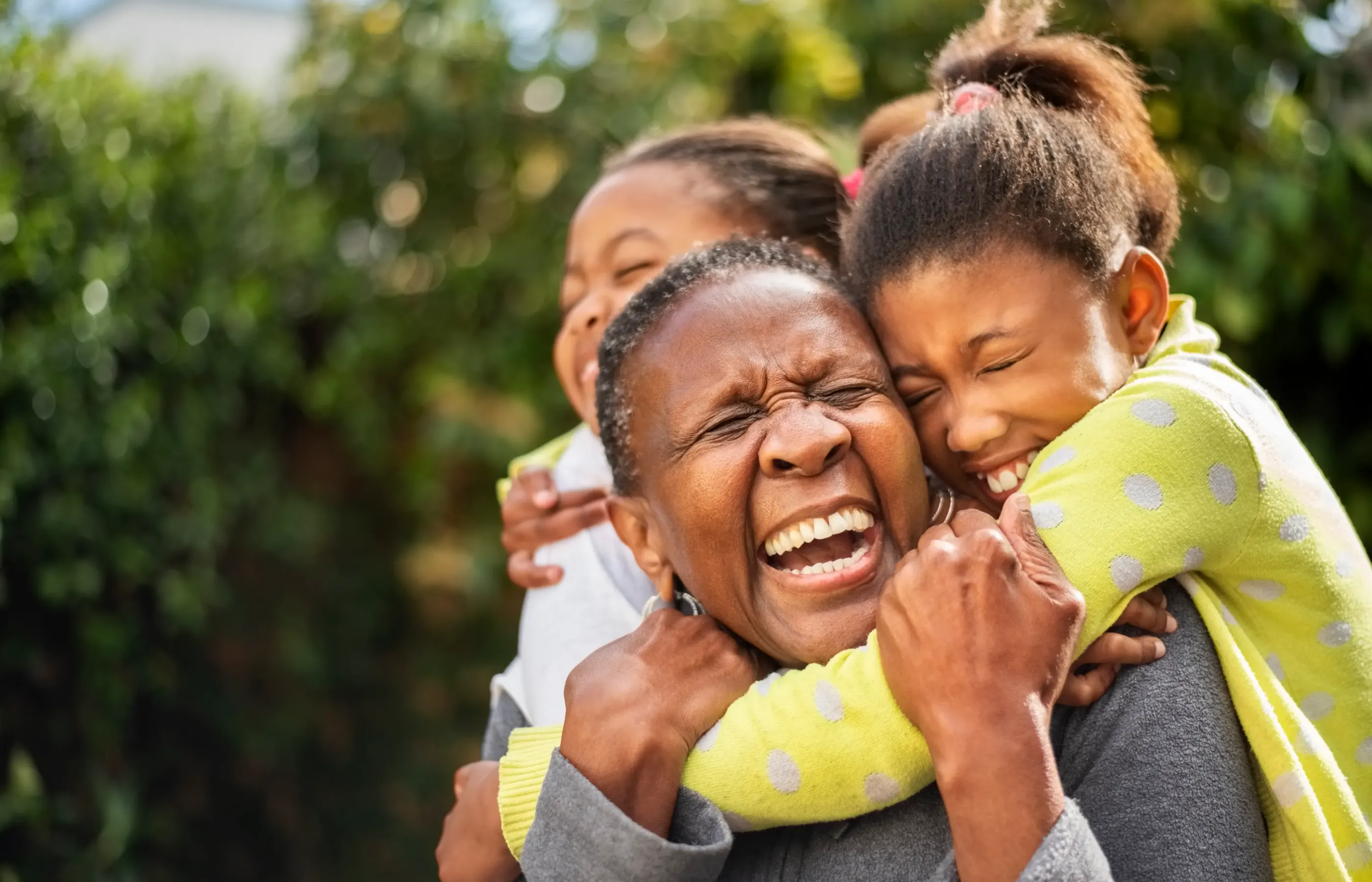 A woman being hugged by two children while they are all smiling and laughing.