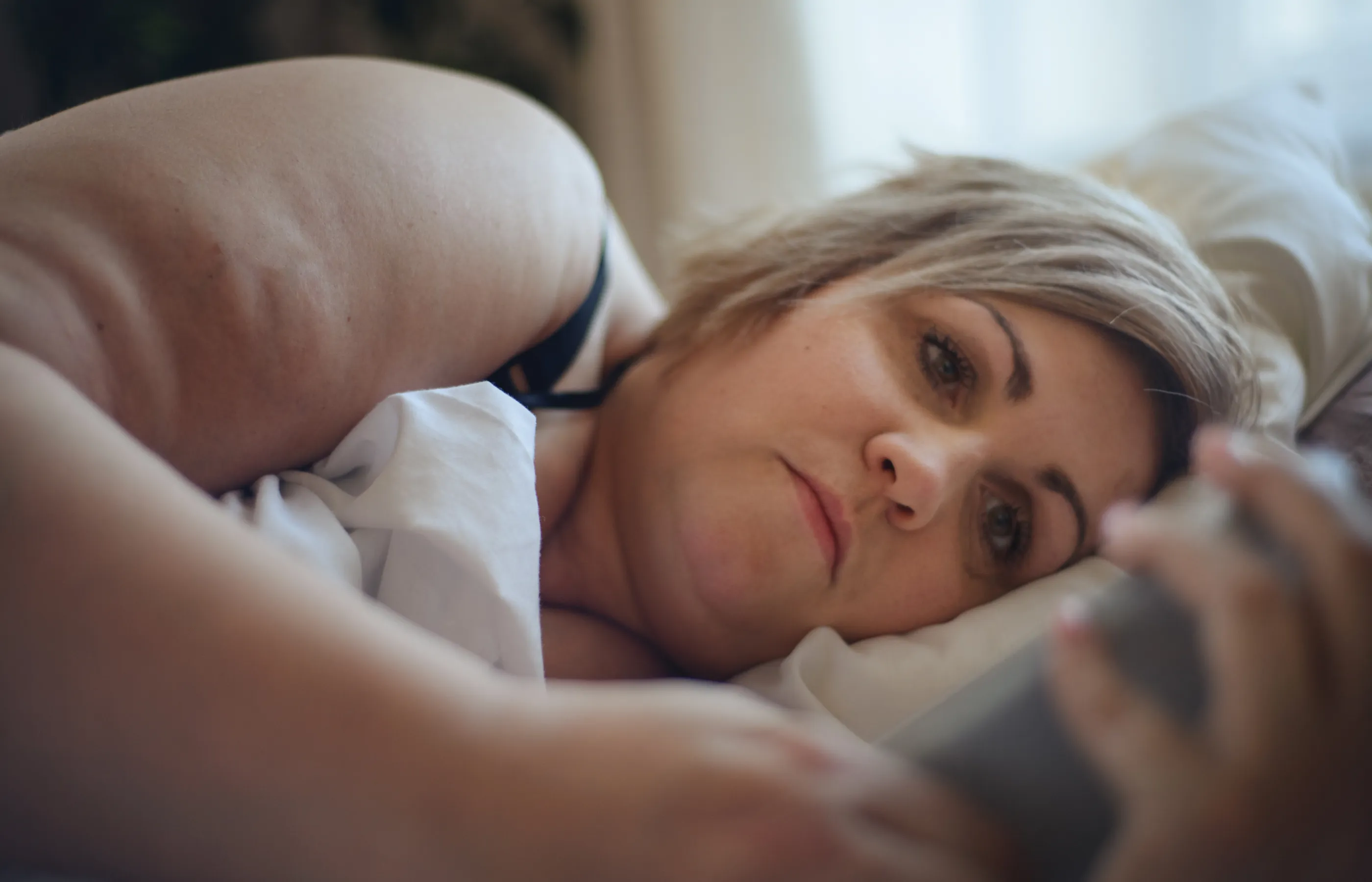 A woman is lying in the bed while looking at her smart phone. 