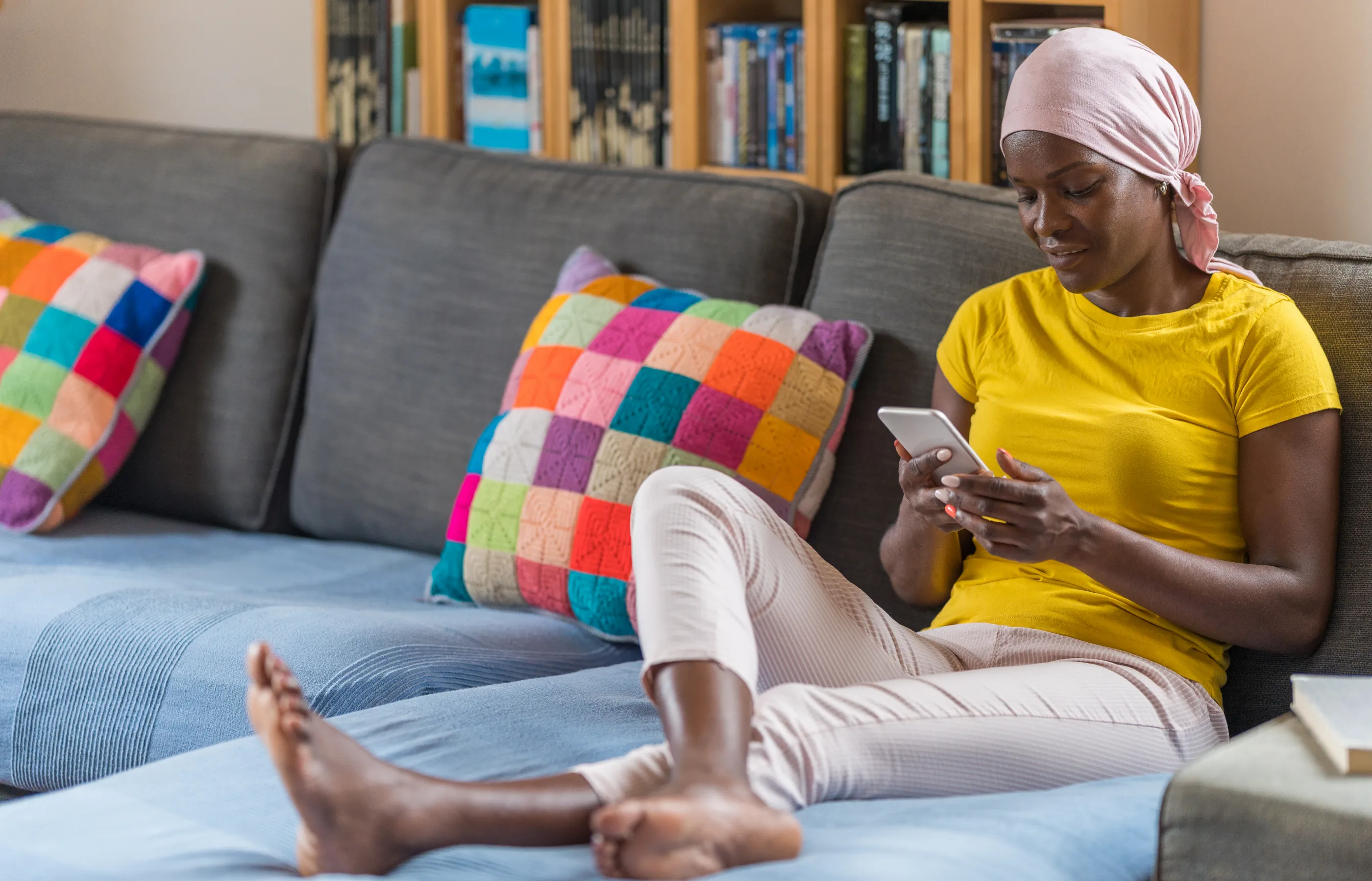 A Cancer patient is home, sitting on her sofa, browsing on her smartphone. 