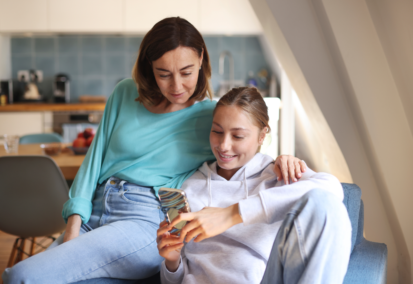 A mother embraces her daughter while they look at a smart phone.