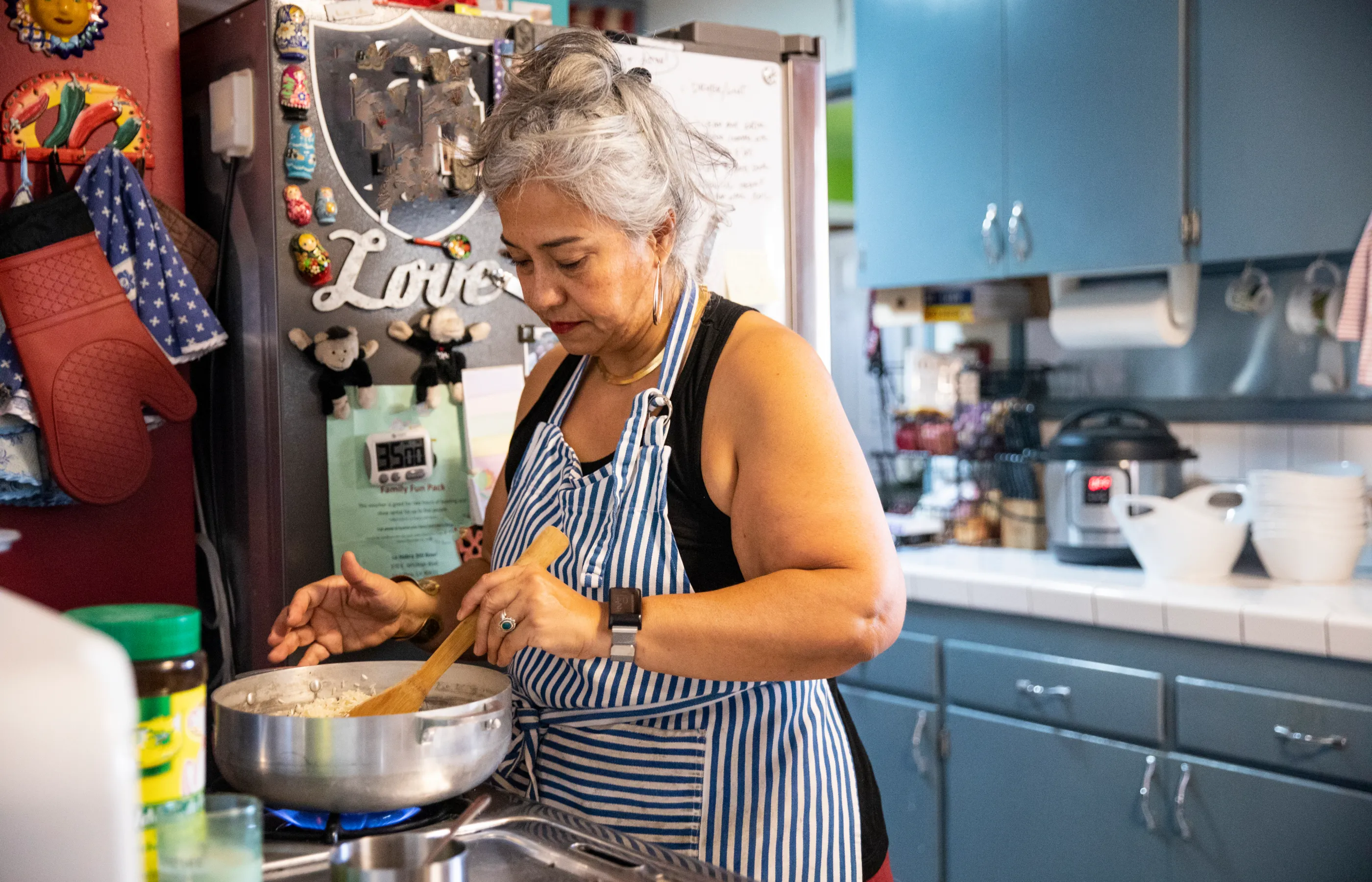 Senior woman, in her home kitchen, with an apron on cooking. She's standing over the stove and stirring the food in a pot. 