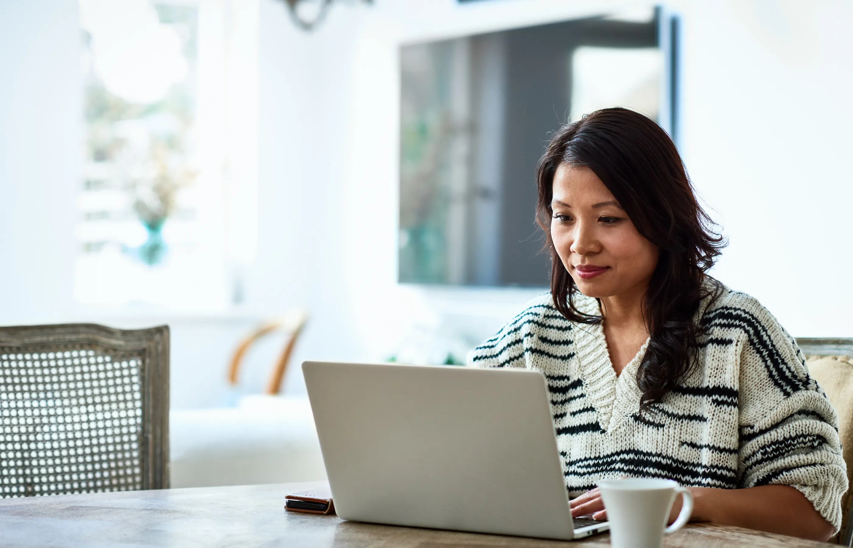 A woman is sitting a table with her laptop and coffee. 