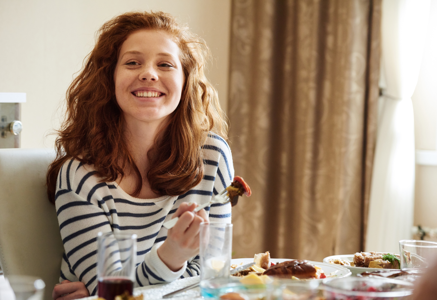 A young woman smiles while sitting at a dinner table with food.