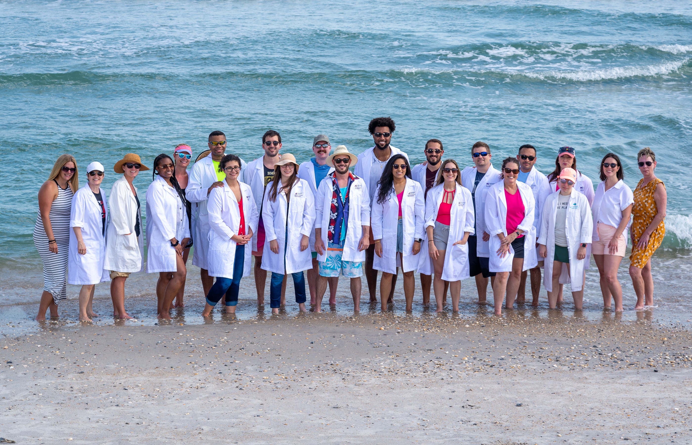 A group of residents standing together in their lab coats on the beach. 