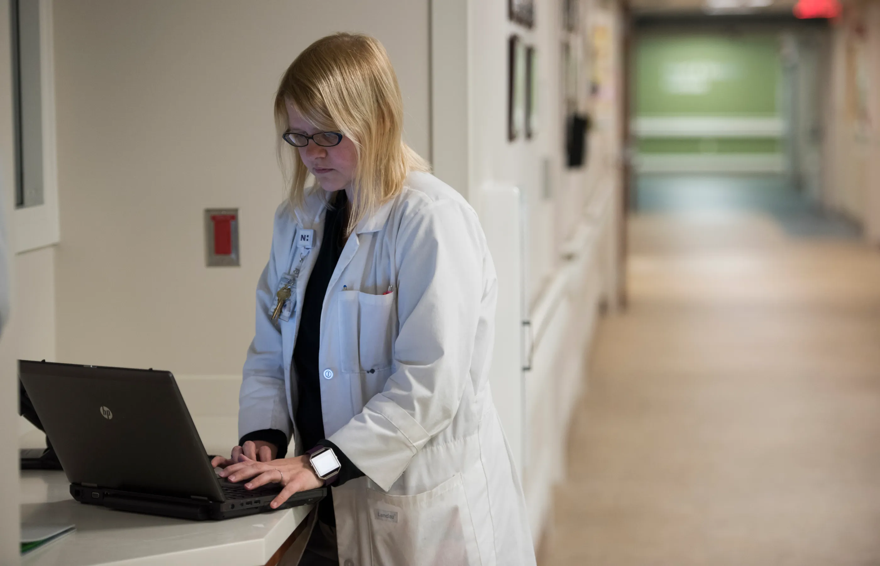 A Novant Health doctor is in the hallways of a hospital typing on a laptop.