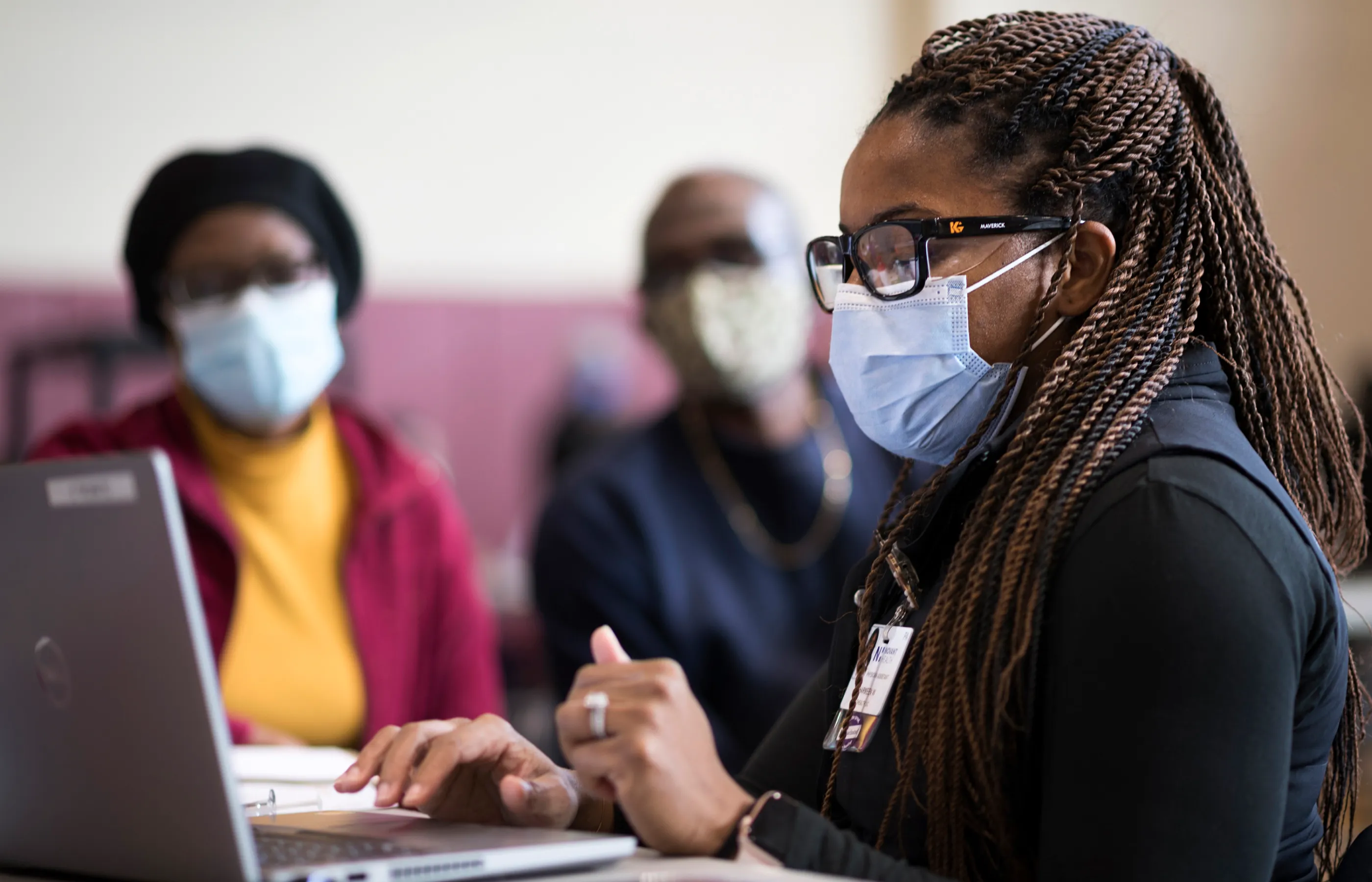 Novant Health team member and couple at a community care event. Everyone is masked and the team member is gathering information on a laptop. 